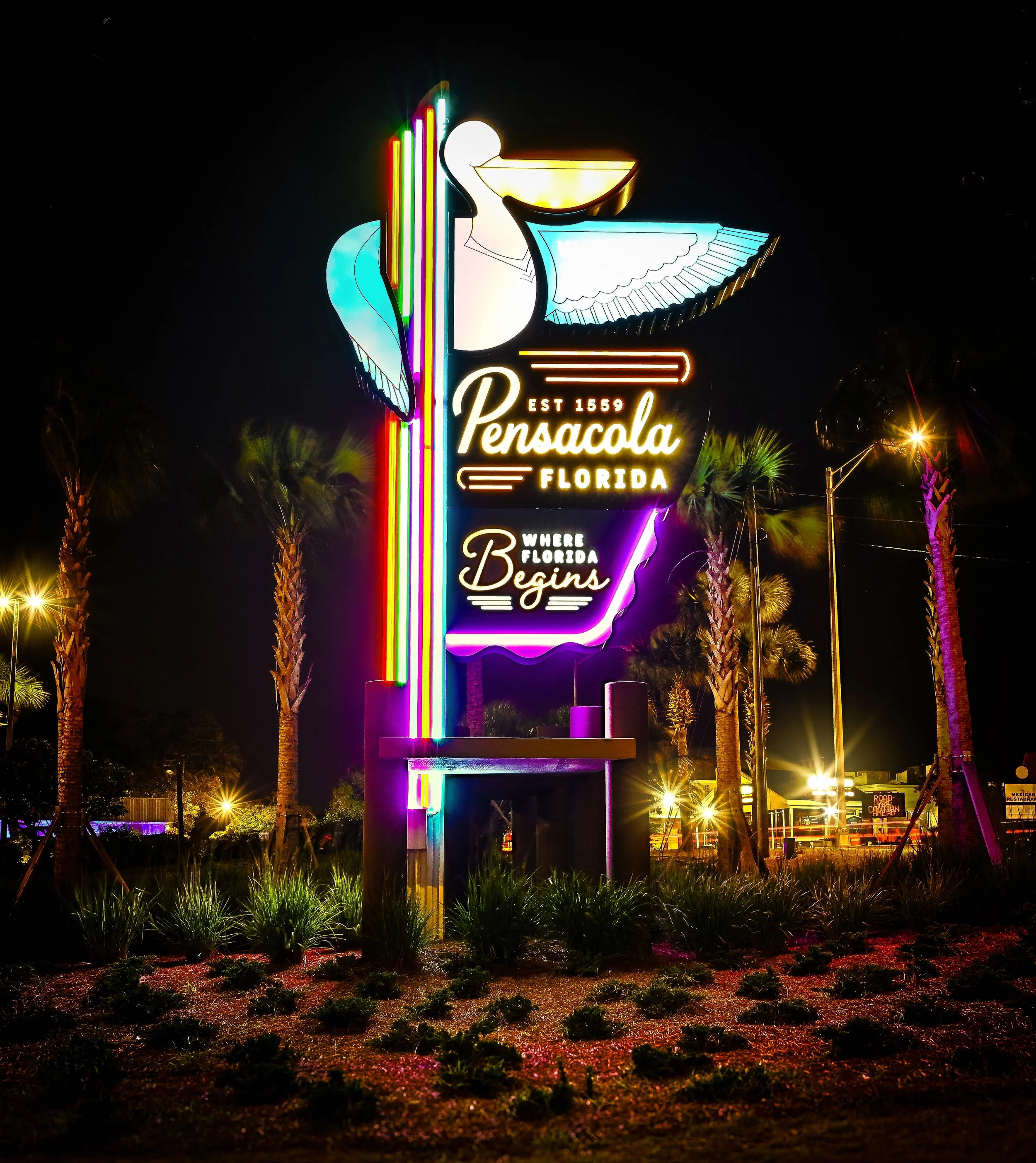 Colorful illuminated Pensacola, Florida welcome sign at night, surrounded by palm trees.