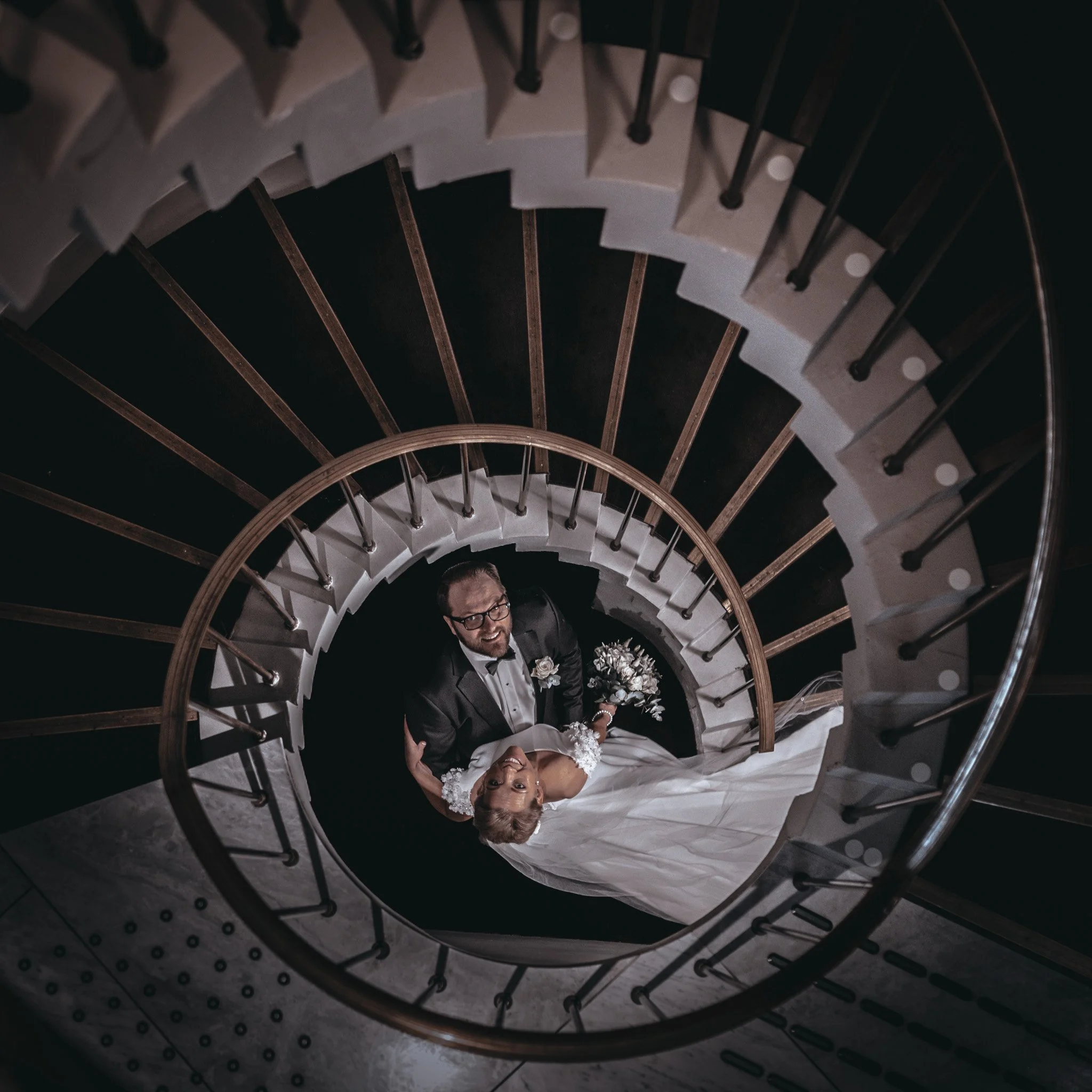 Bryllupsfoto/video: Brudepar står nederst i en spiraltrapp, sett fra oven.