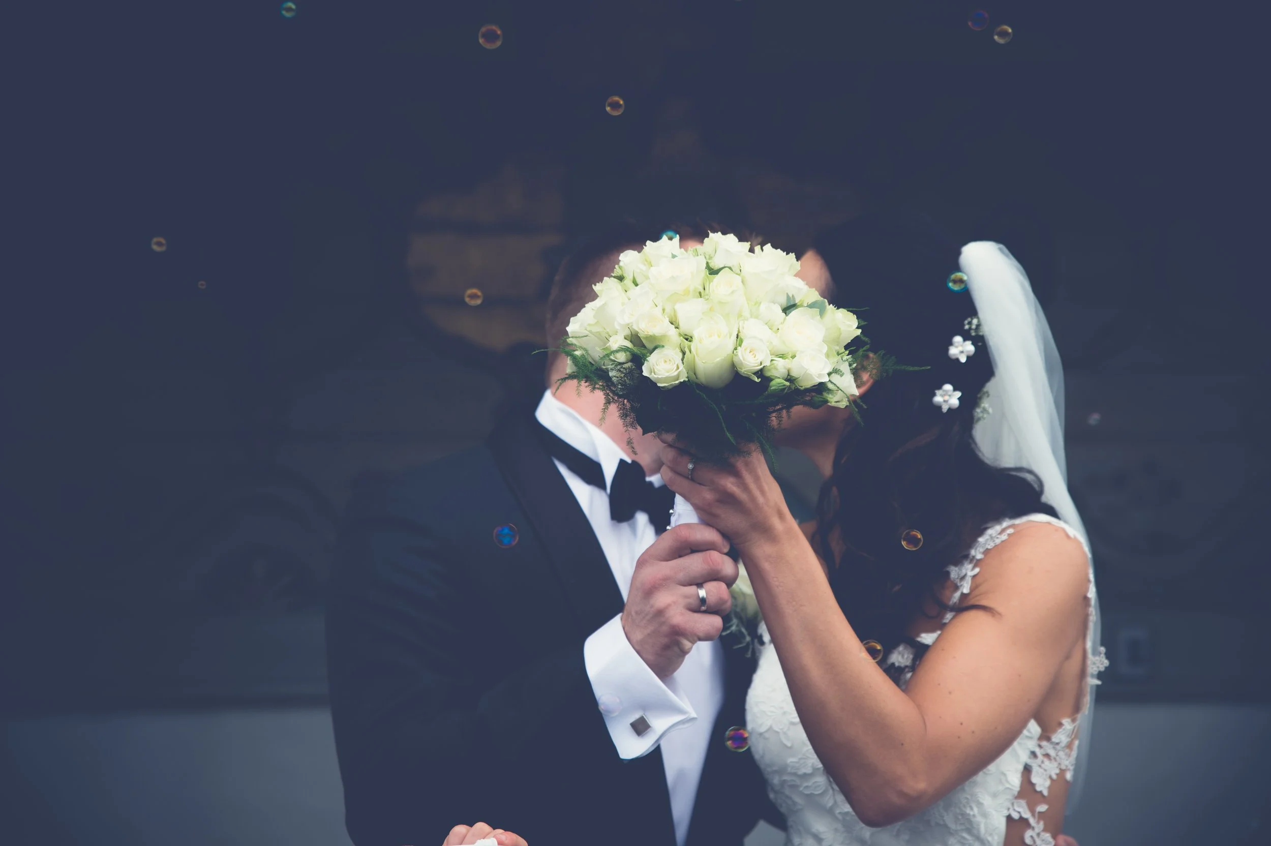 Bryllupsfoto/video: Brudepar som kysser bak en bukett med hvite roser.