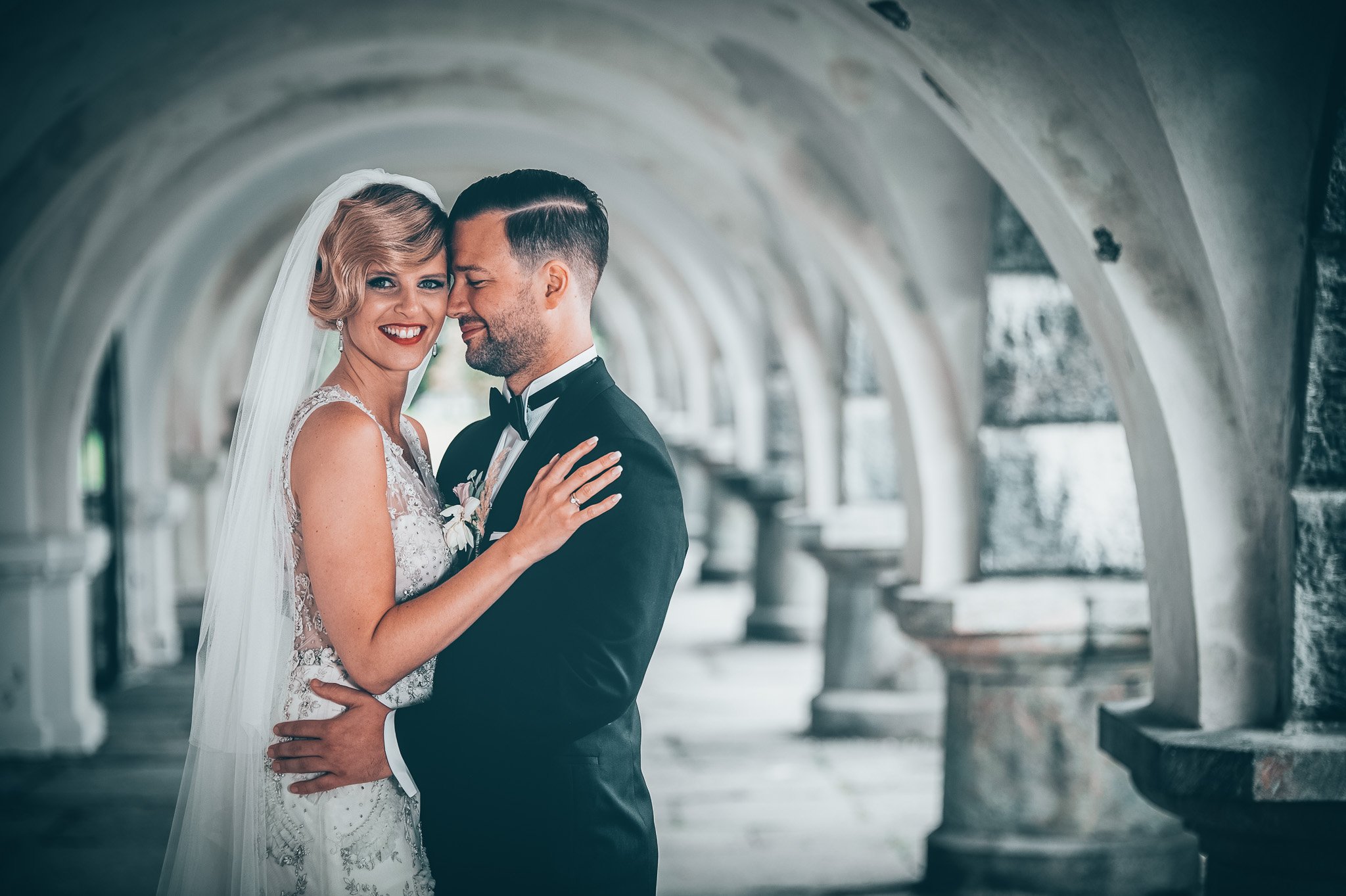 Bryllupsfoto/video: Brudepar i en elegant arkade, smilende og kledd i bryllupsklær.