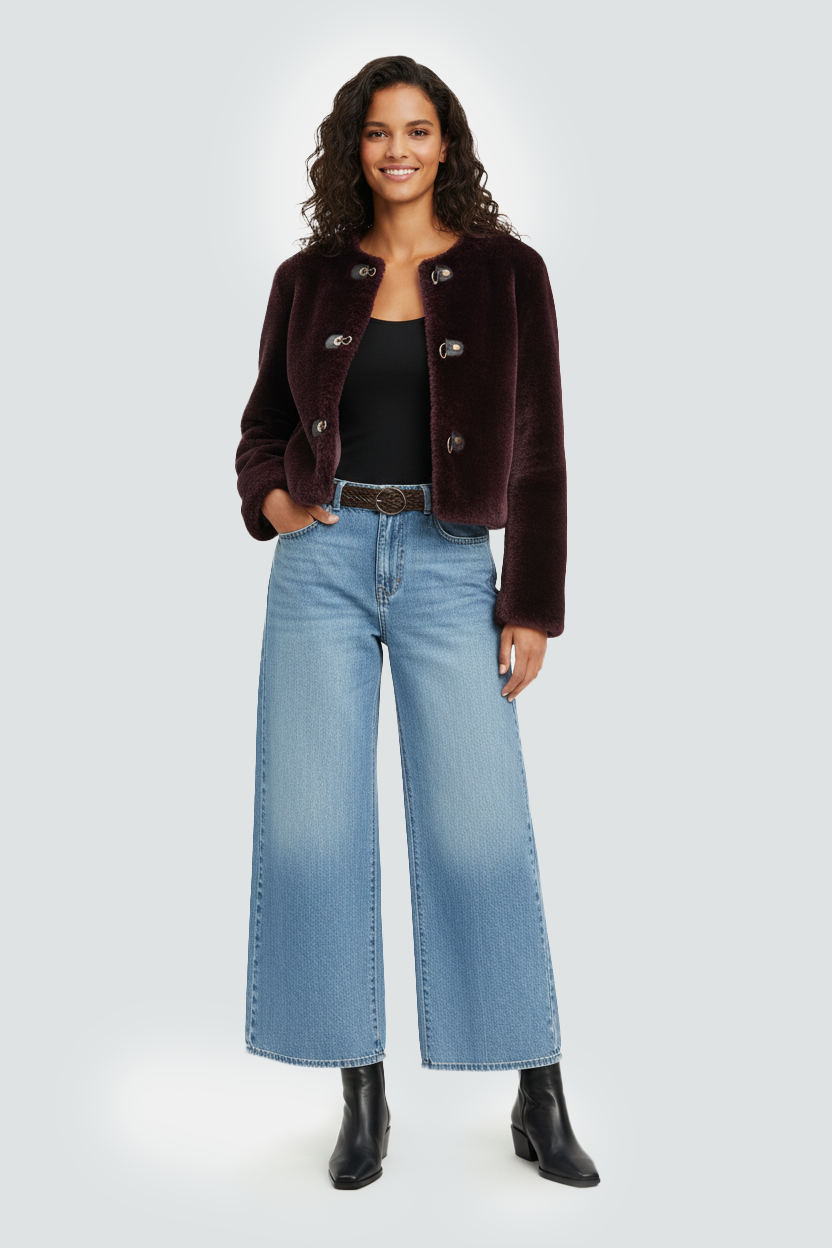 Image IA mode d'une Femme souriante portant une veste en velours bordeaux, un t-shirt noir, un jean large bleu clair, et des bottines noires, debout contre un fond clair.