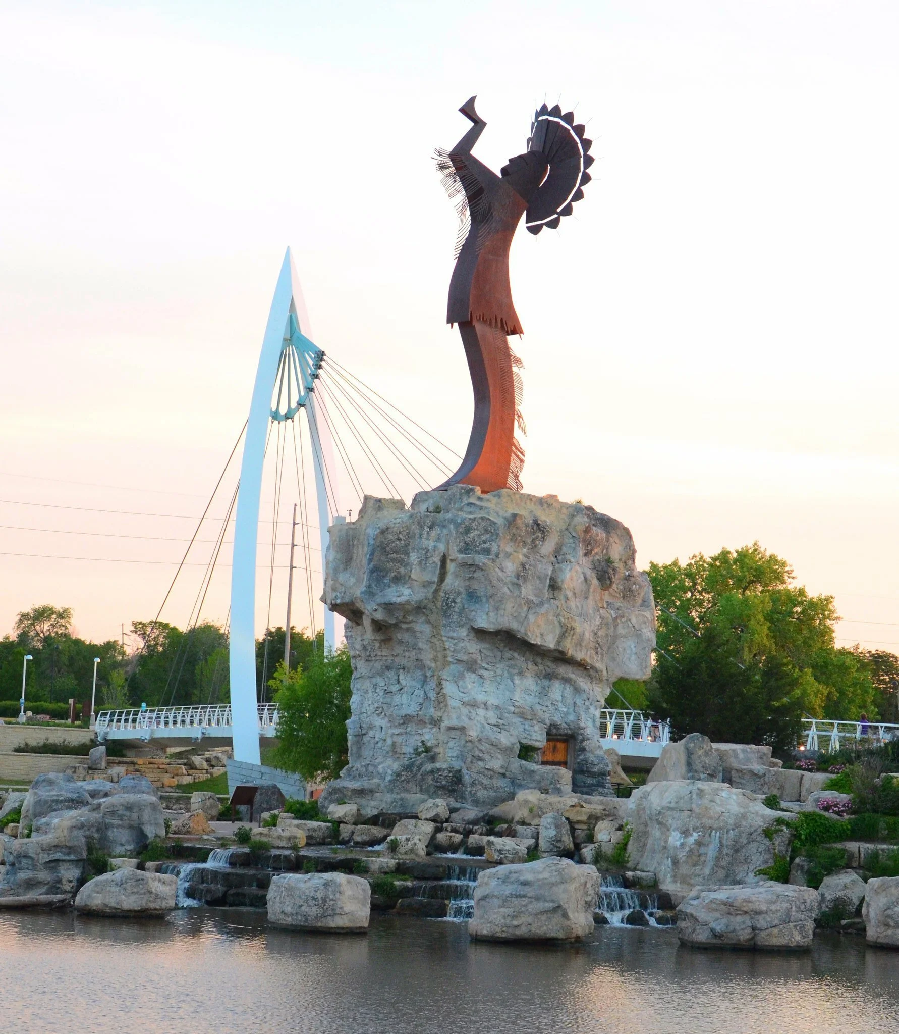 Photo of iconic Wichita (KS) sculpture: an Indian Chief in full headdress with hands lifted to the sky, on a stone pedestal