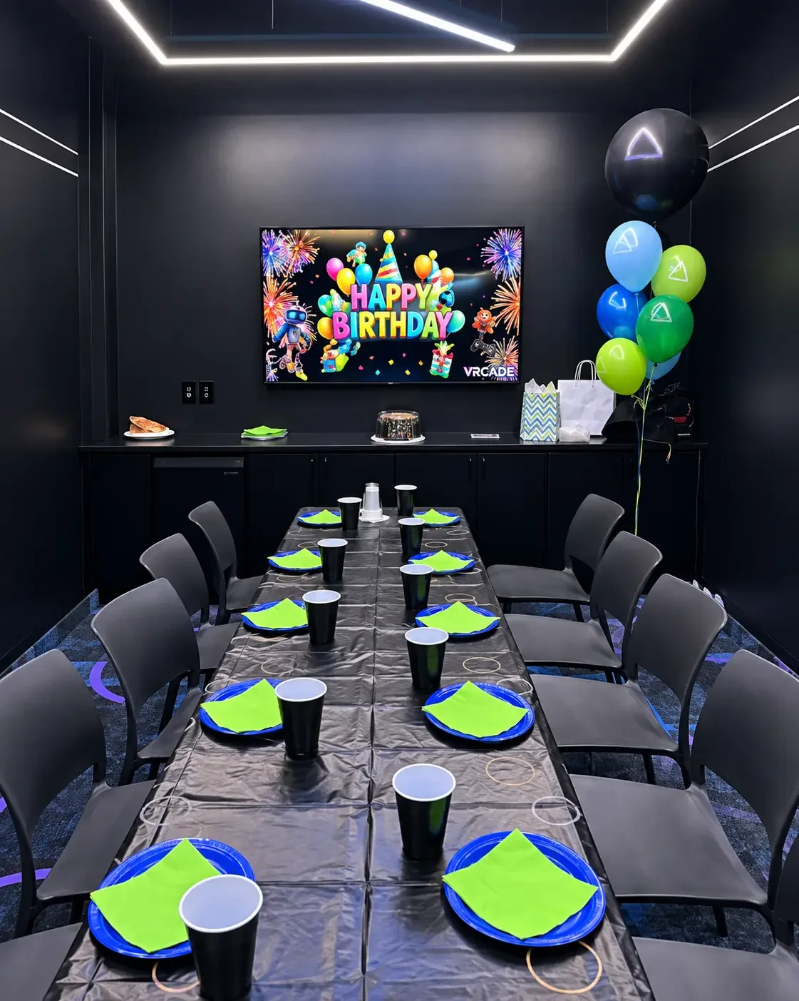 Private birthday party room at VRCADE in Scarborough prepared with a long table, blue plates, green napkins, balloons and a Happy Birthday TV display.