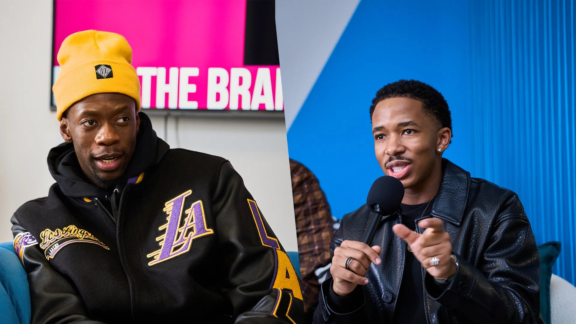 Two men are speaking into microphones during an interview or discussion. The man on the left wears a yellow beanie and a black jacket with purple and gold logos, with a pink and white background behind him. The man on the right wears a black leather jacket, has short curly hair, and is pointing as he talks, with a blue background behind him.