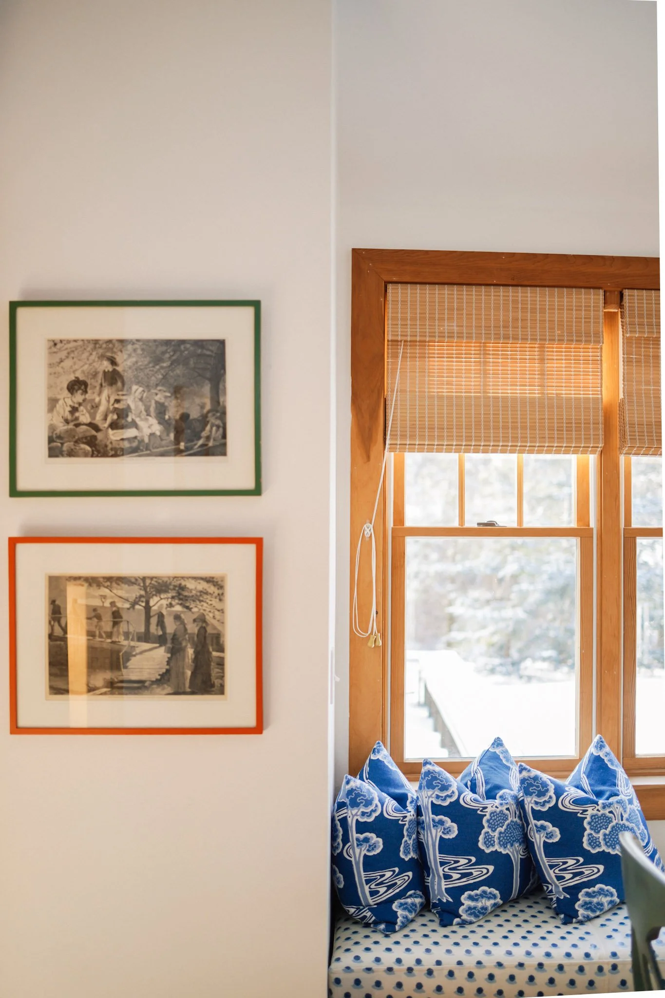 Corner of a cozy room with a built-in window seat, blue and white cushions, black and white framed artwork, and a view to an outdoor patio