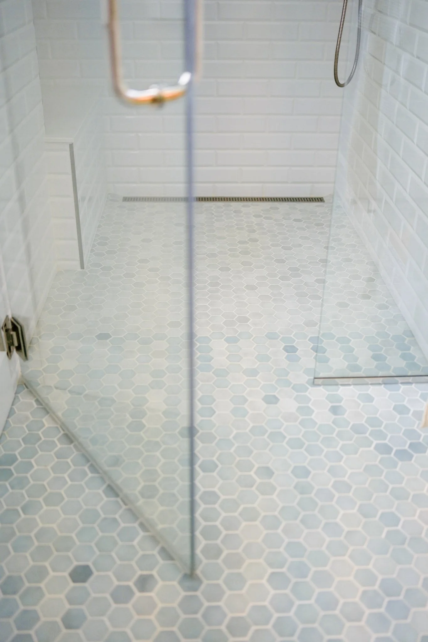A walk-in shower with a rain shower head, white brick walls, and light gray hexagonal floor tile