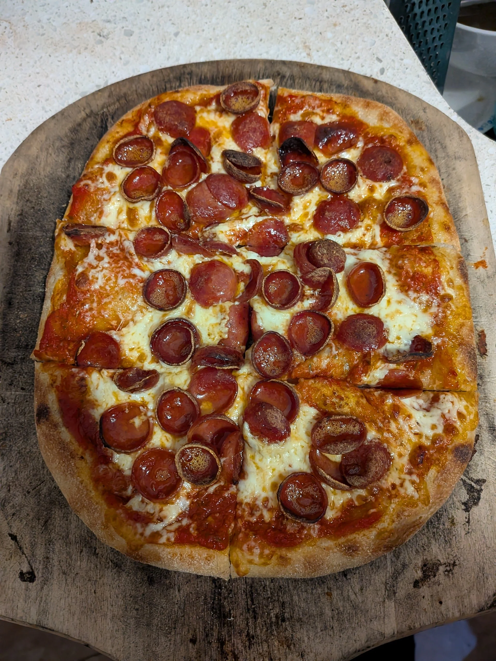 A pepperoni pizza on a wooden pizza peel with four slices removed, sitting on a light-colored countertop