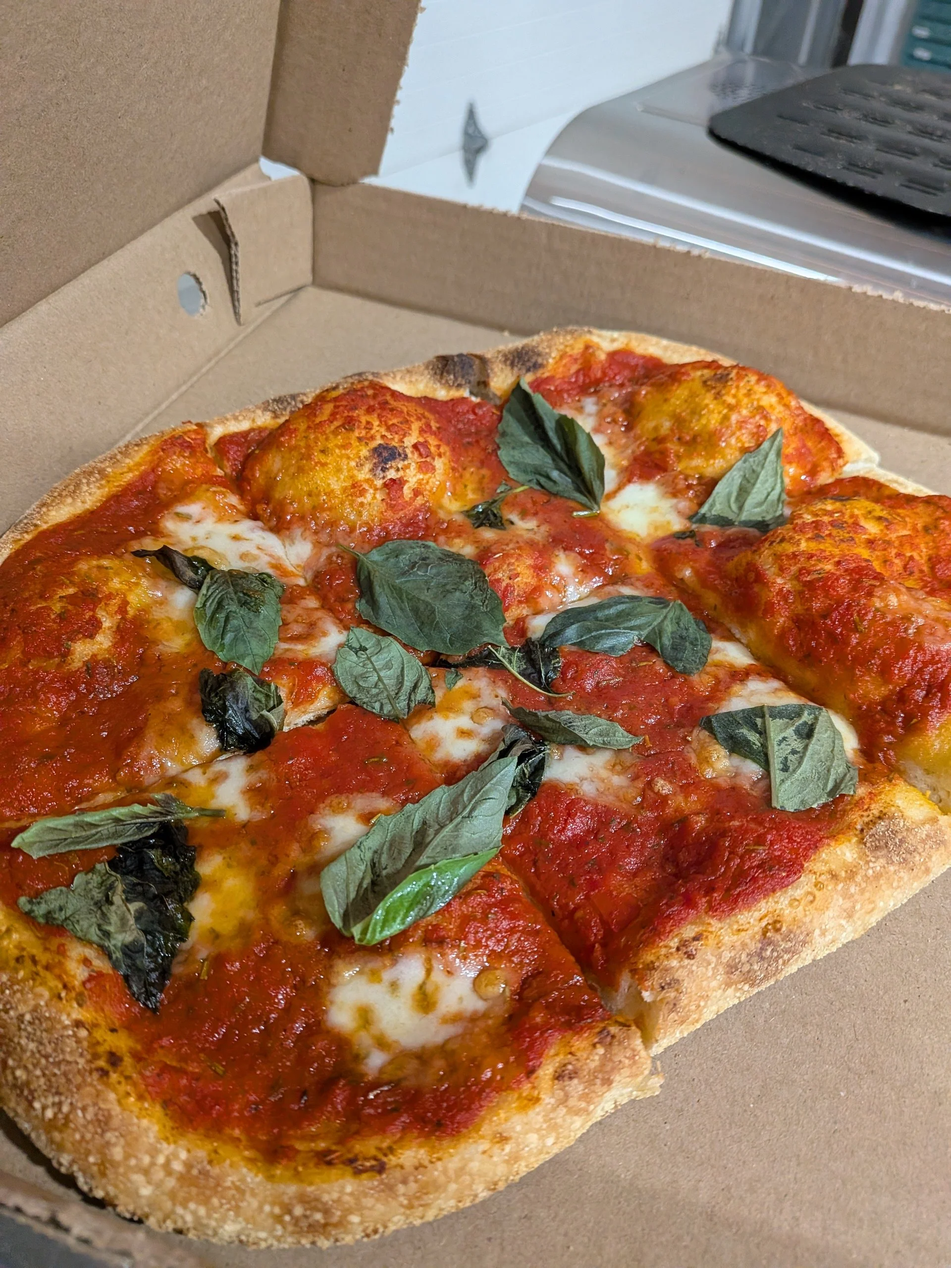 A cheese pizza topped with fresh basil leaves in a cardboard pizza box.
