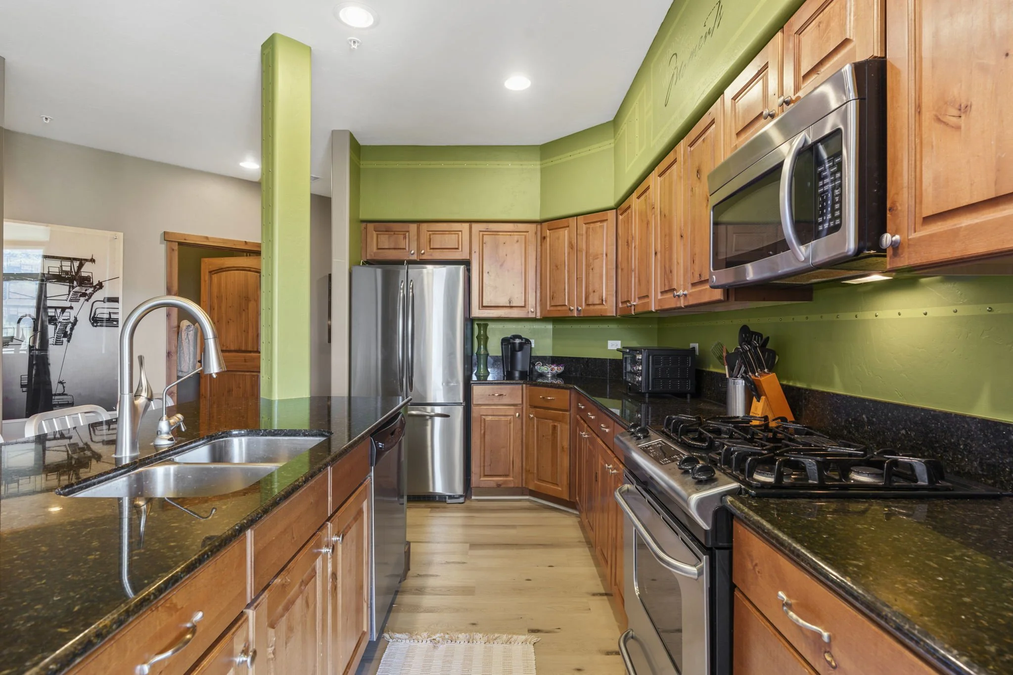 A kitchen with green walls, wooden cabinets, black granite countertops, stainless steel appliances, a gas stove, and a double sink.