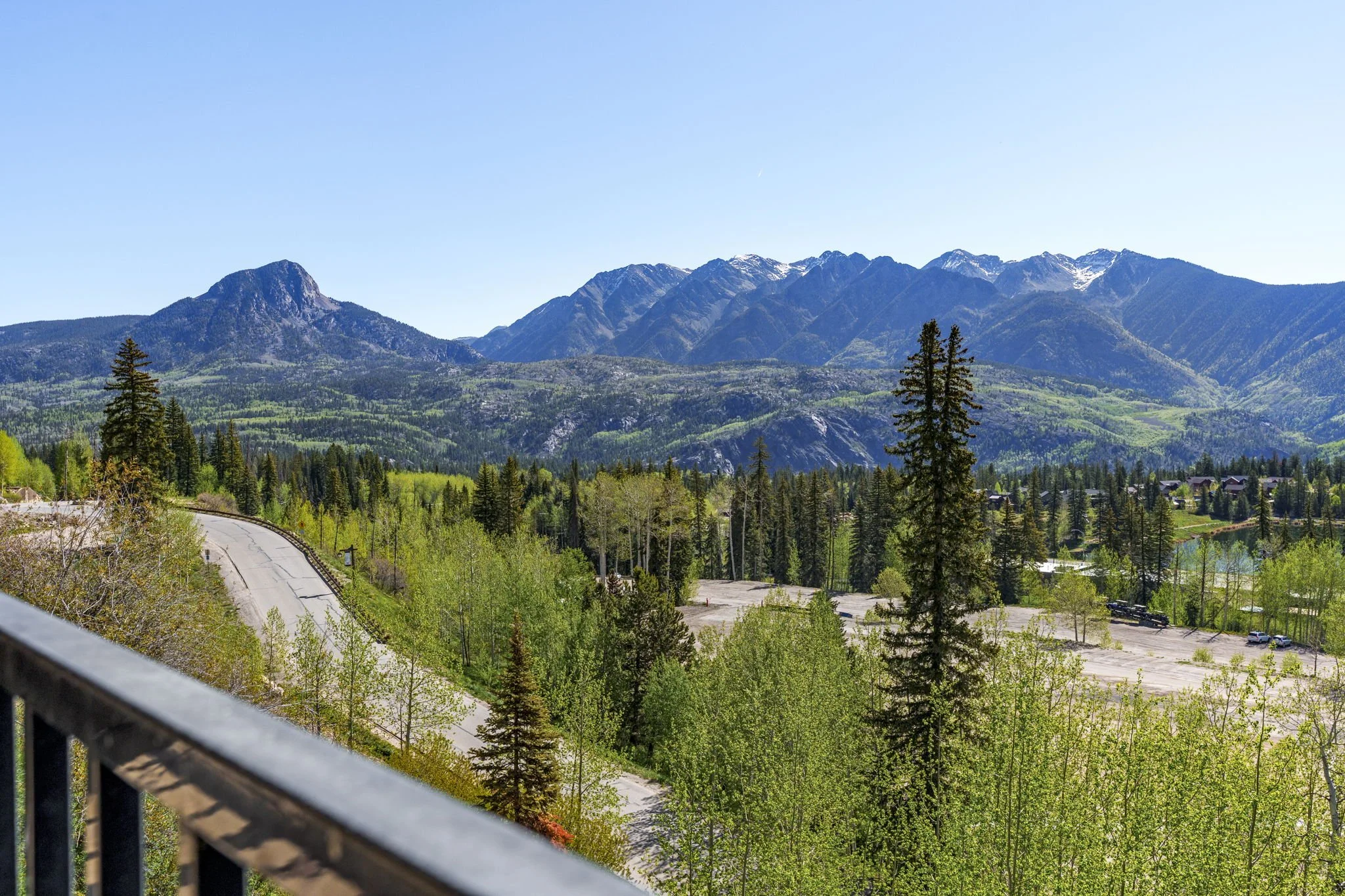 Scenic view of a mountain range with lush green forest at the base and snow-capped peaks in the distance, under a clear blue sky.