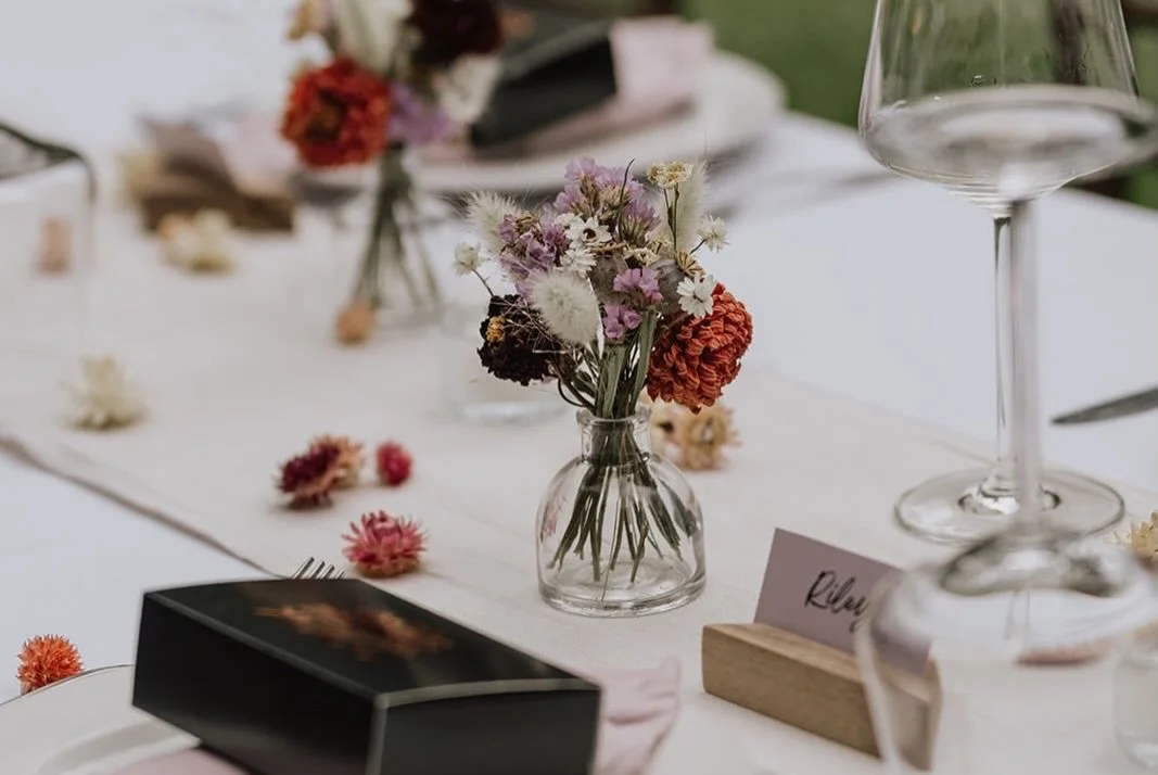 A table set for a gathering with a small glass vase of mixed pink, white, and orange flowers.