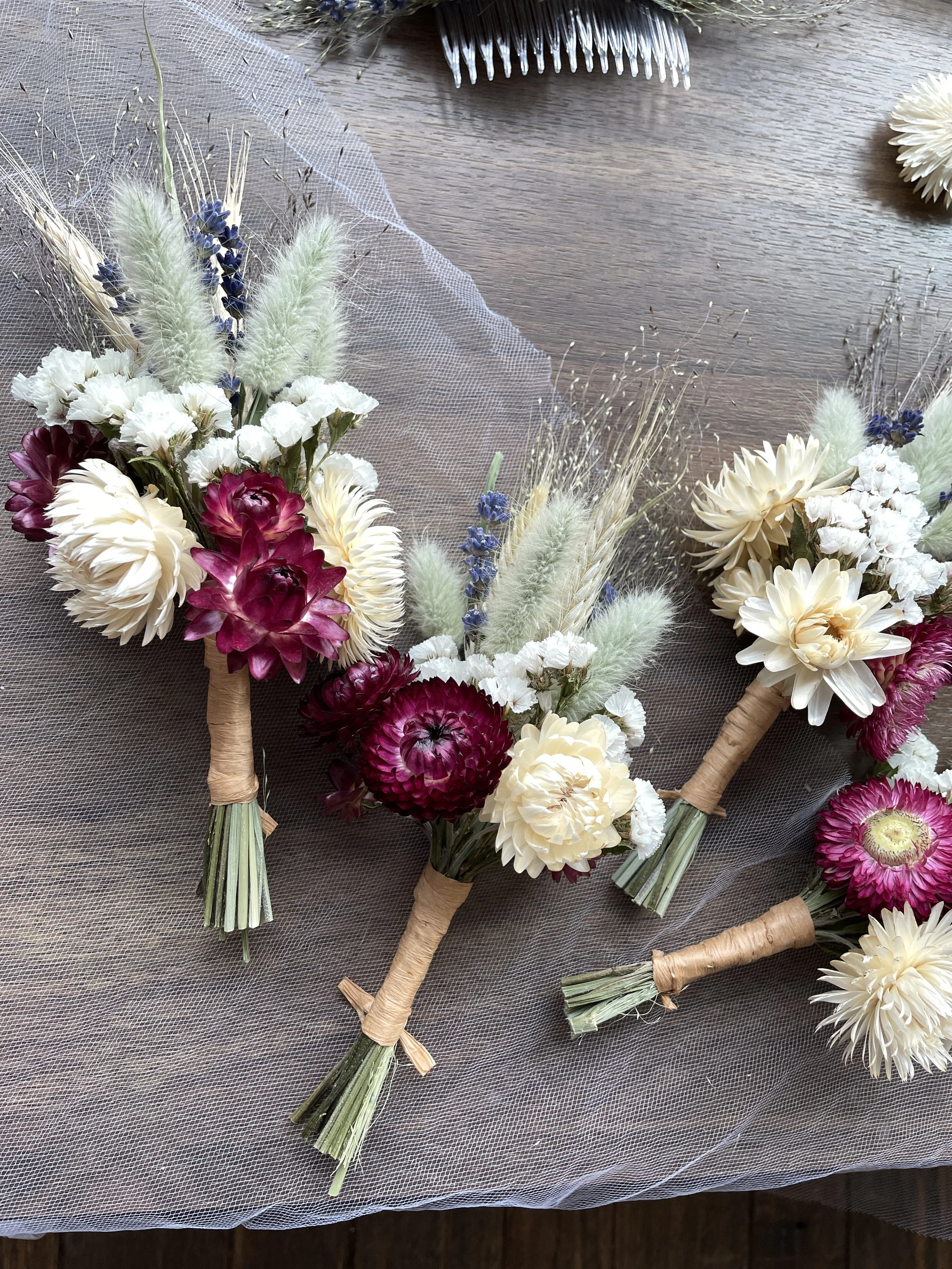 A close-up of several handmade floral boutonnieres with a mix of white, purple, and cream-colored flowers, all tied with twine.