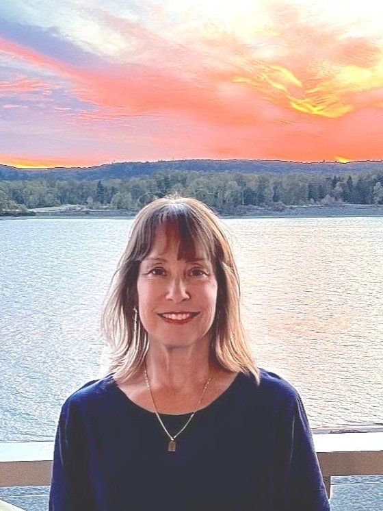 A woman standing on a balcony with a scenic view of a lake at sunset.