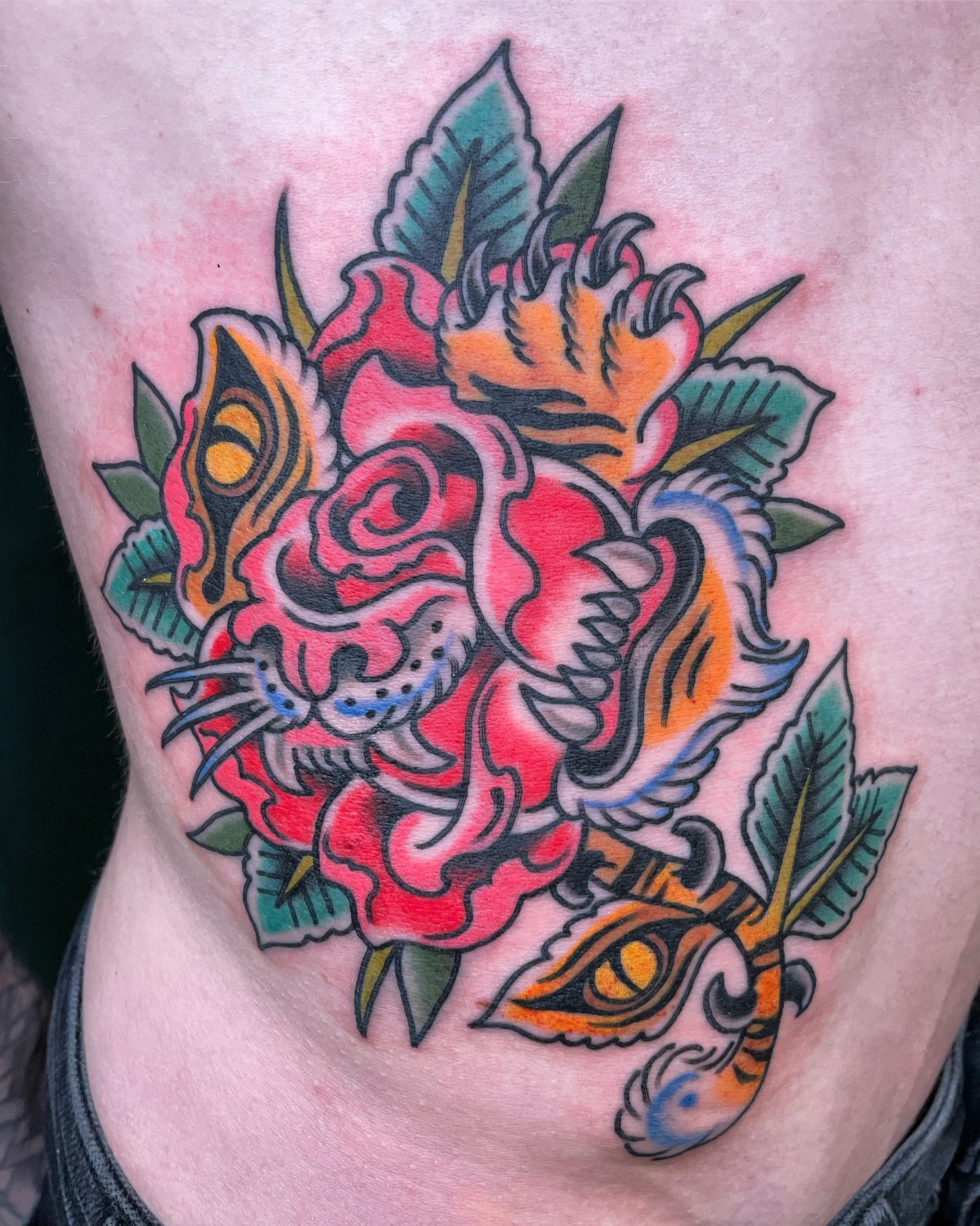Colorful tattoo of a tiger face intertwined with roses and leaves, featuring bold outlines and vivid colors.