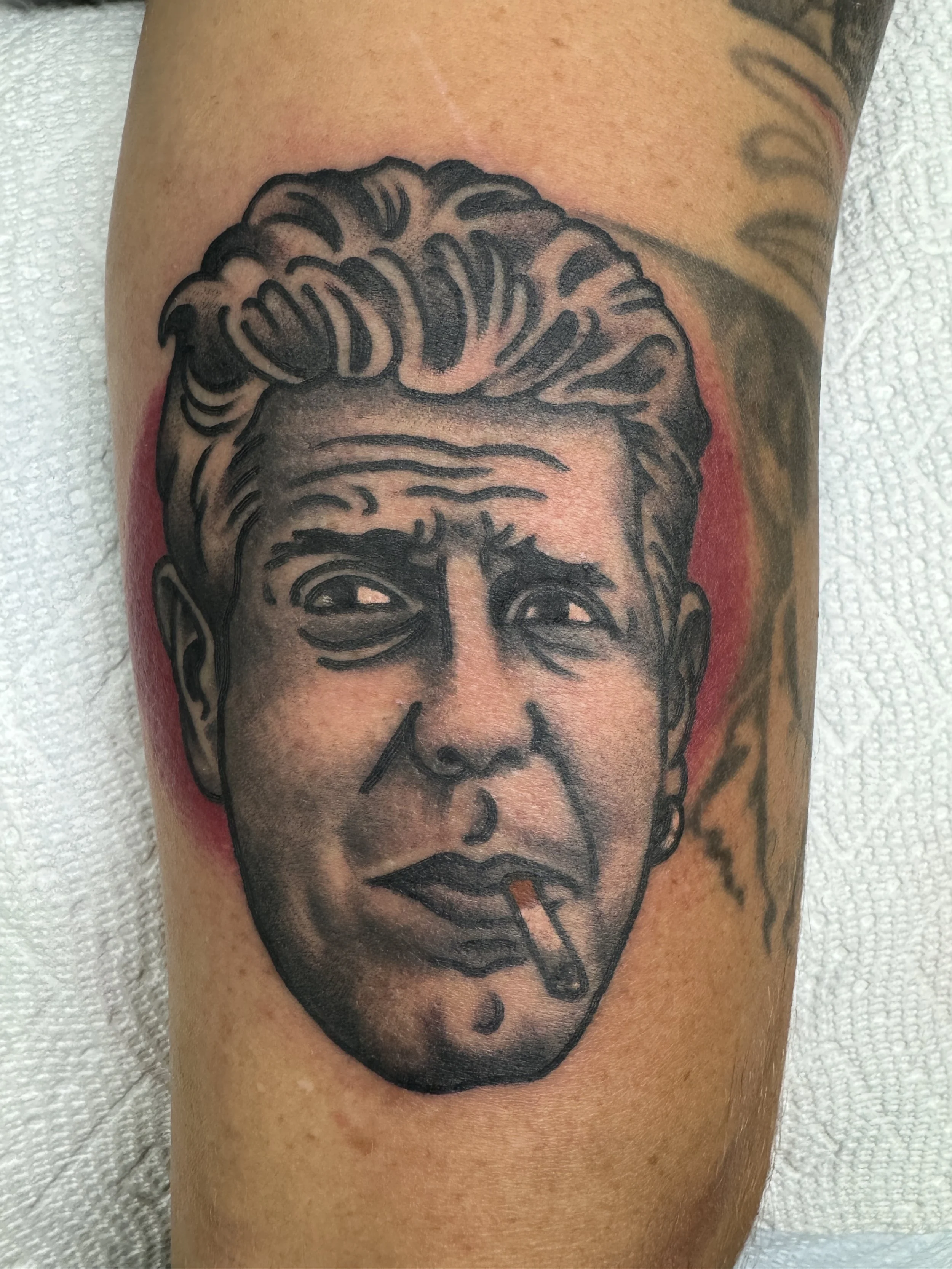 Tattoo of a black-and-gray portrait of a man with a cigarette in his mouth on skin.