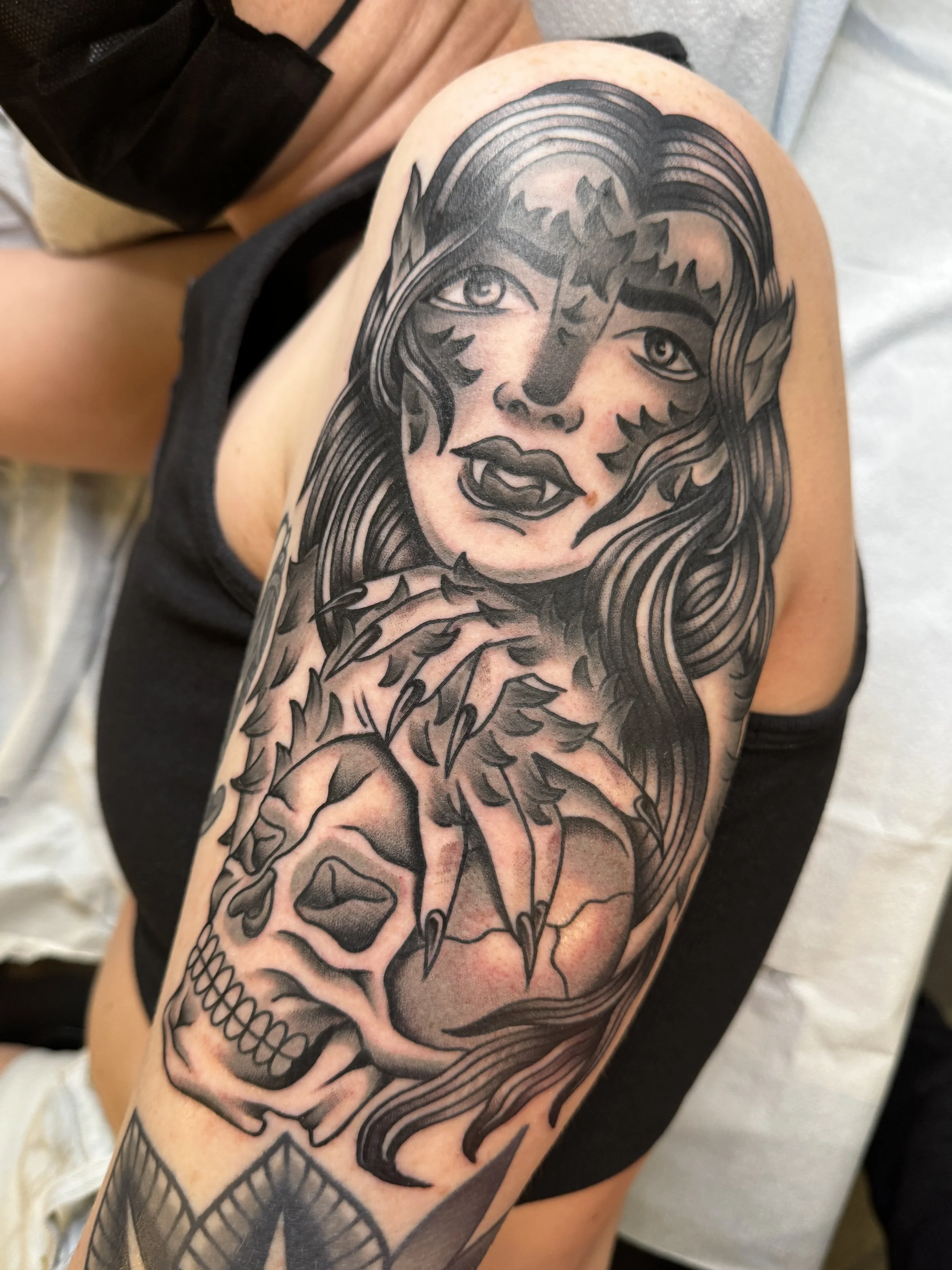 Tattoo of a woman with long hair, partly a skull, with hand claws, on the upper arm.