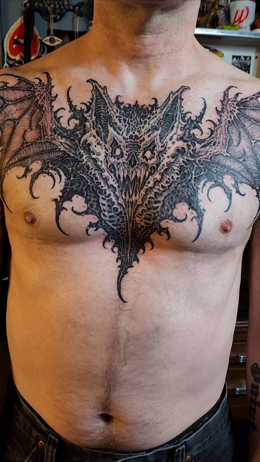 A man's chest tattoo of a detailed demon or dragon face with wings extending onto the shoulders.