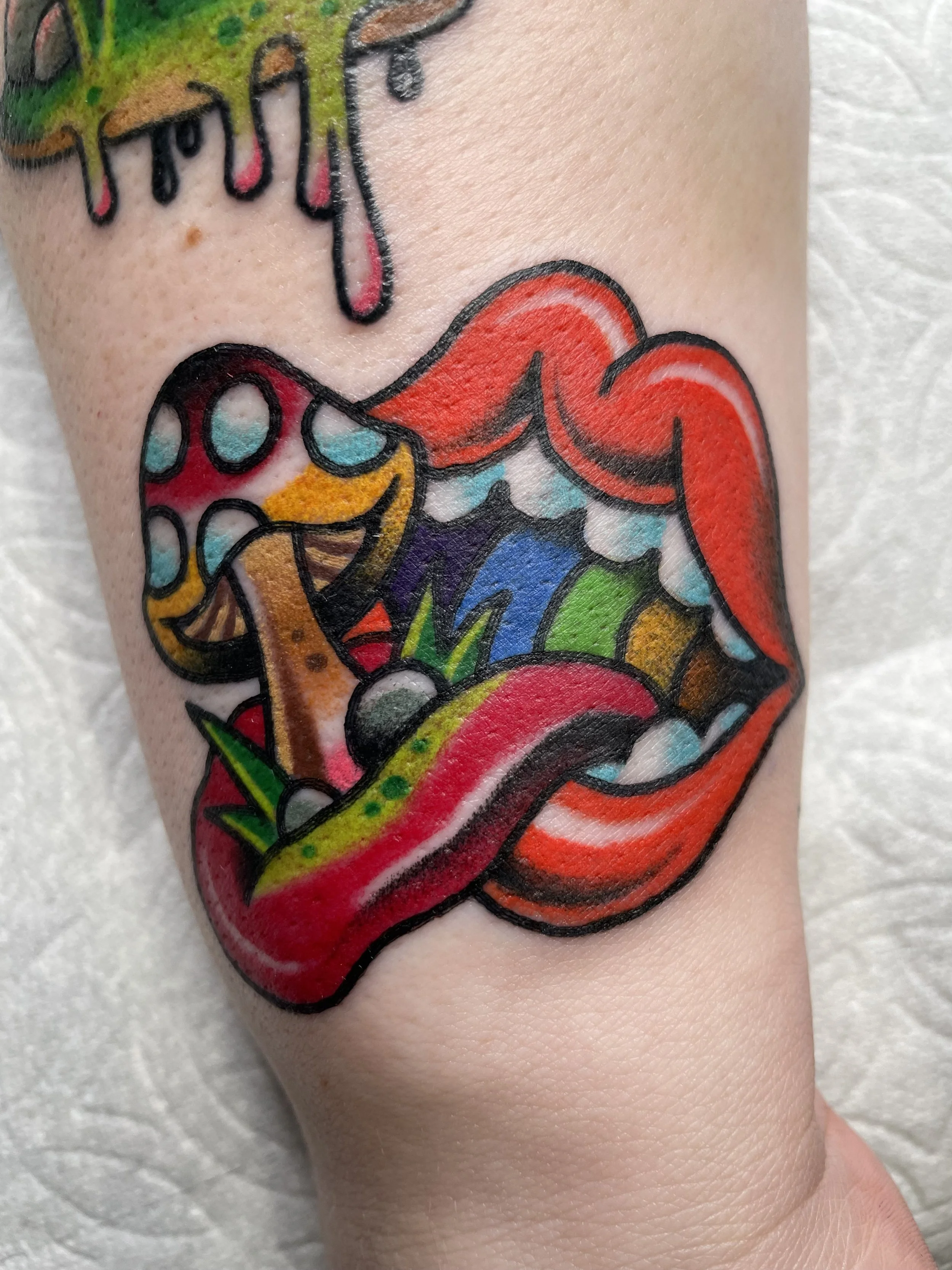 Colorful tattoo of bright red lips with a tongue that is a melting ice cream cone with sprinkles, surrounded by rainbow colors.