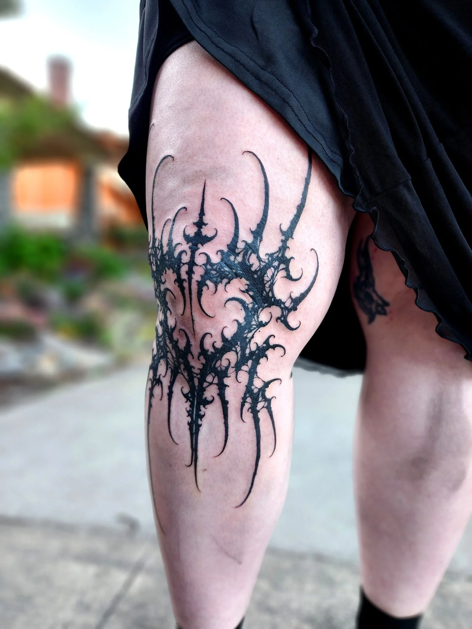 A tattoo of an intricate black abstract design on a person's thigh.