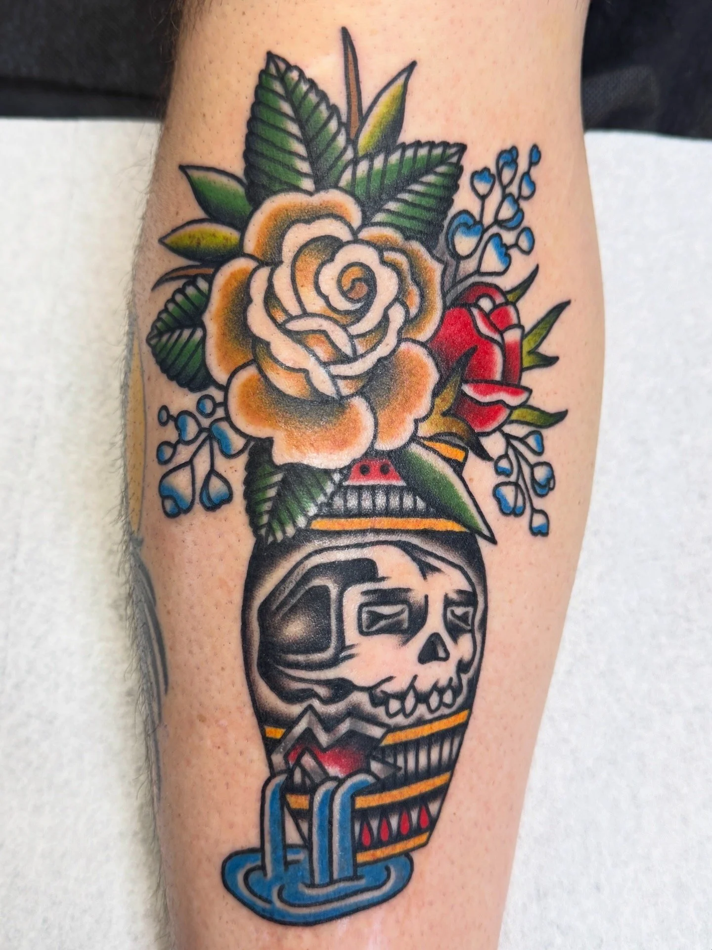Tattoo of a skull in a vase with flowers on the skin.