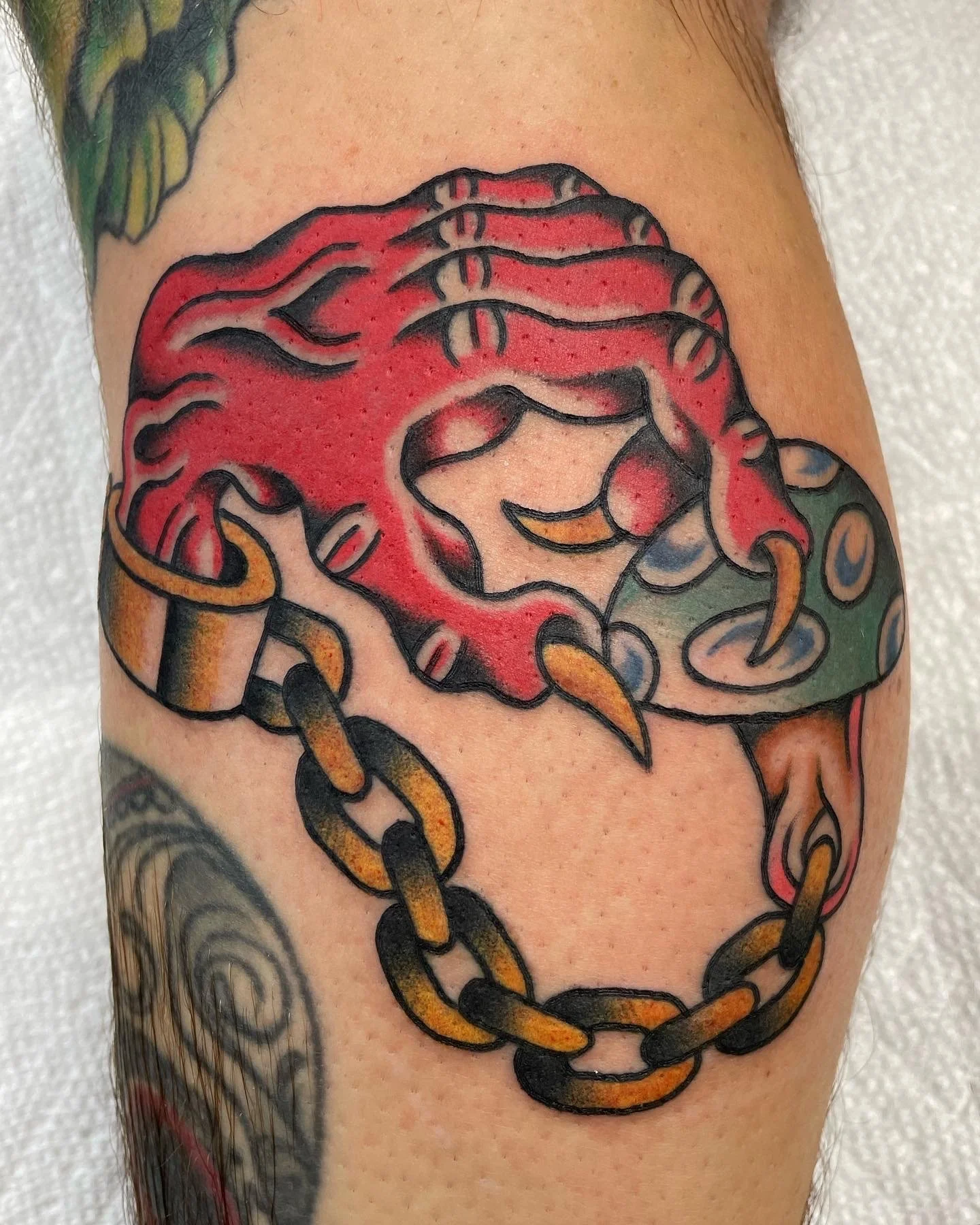 Colorful tattoo of a red skull with a chain hanging from the side on a person's arm.