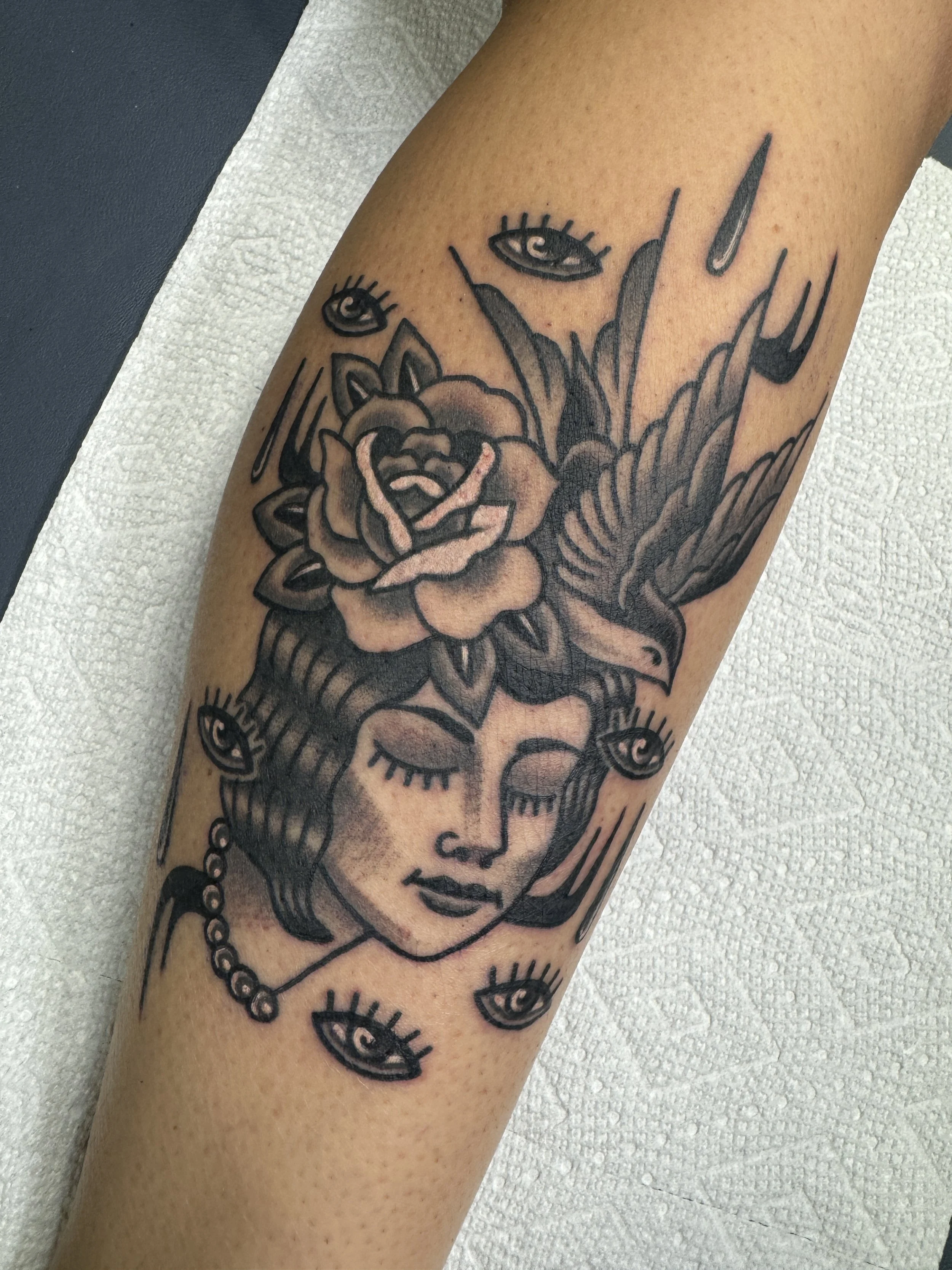 Tattoo of a woman with closed eyes, surrounded by floating eyes, flowers, and a bird on her head.