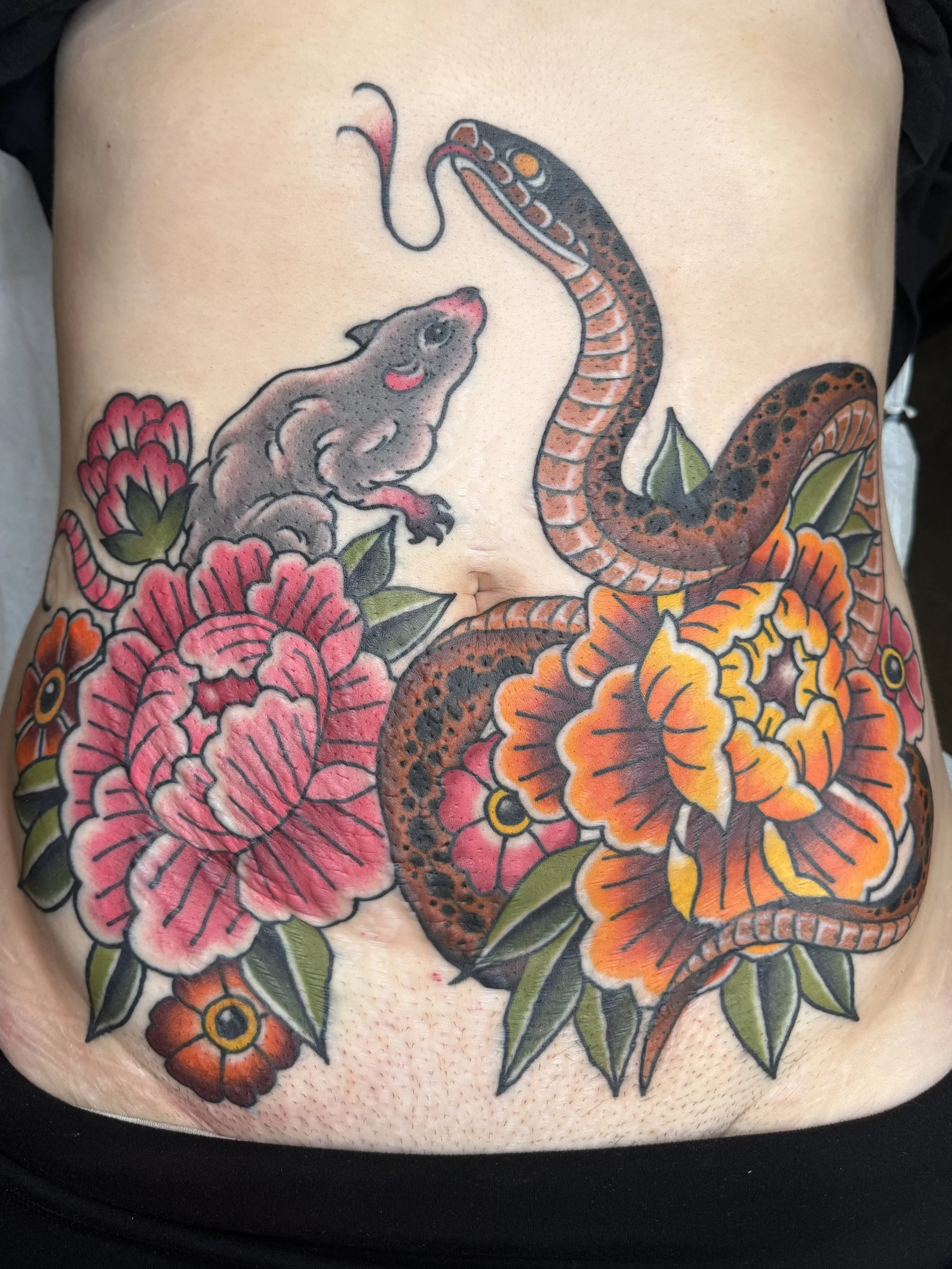 Tattoo of a snake and a rat surrounded by colorful flowers on a person's lower abdomen.