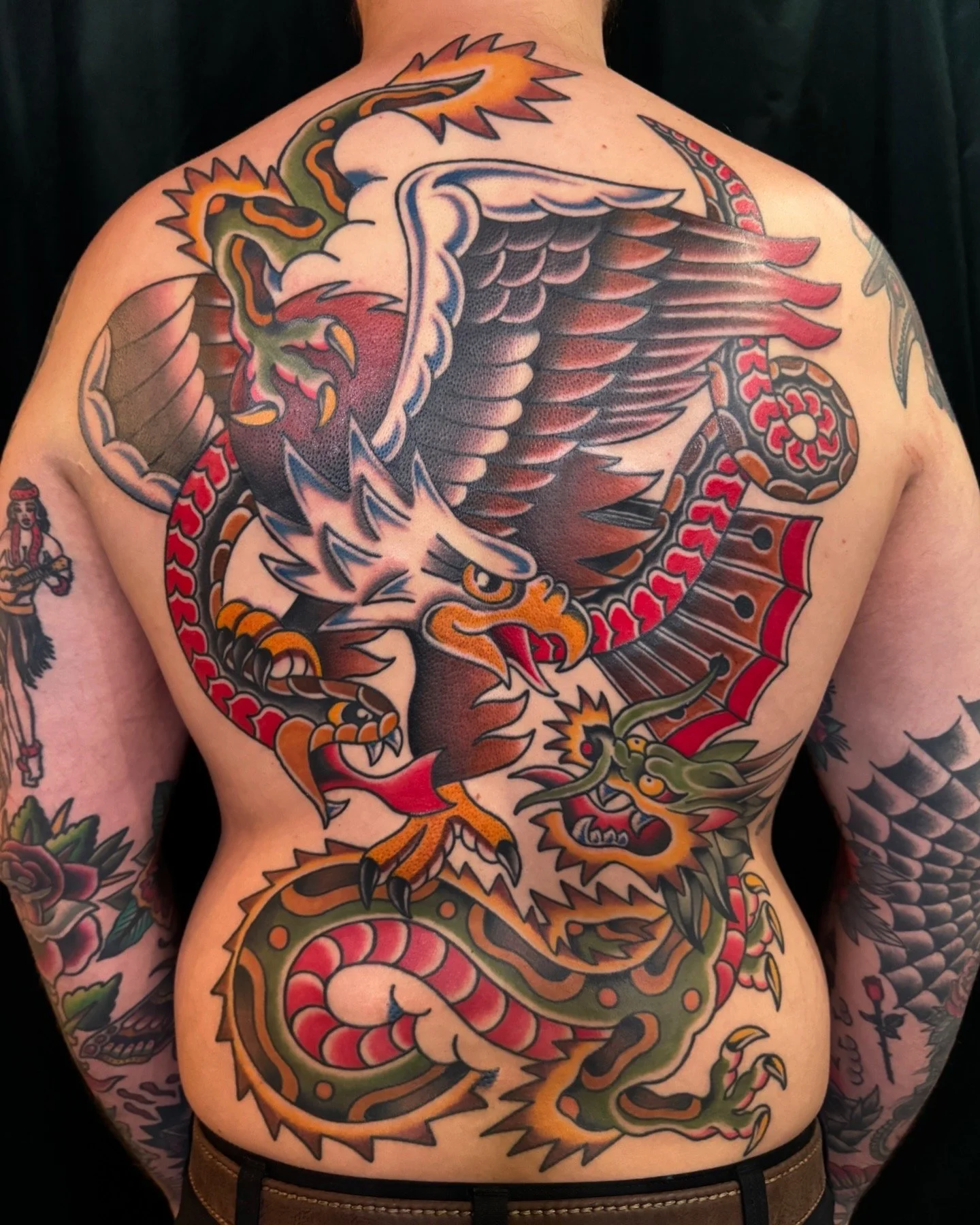 A colorful traditional Japanese style tattoo of an eagle and a dragon on a person's back and arms.