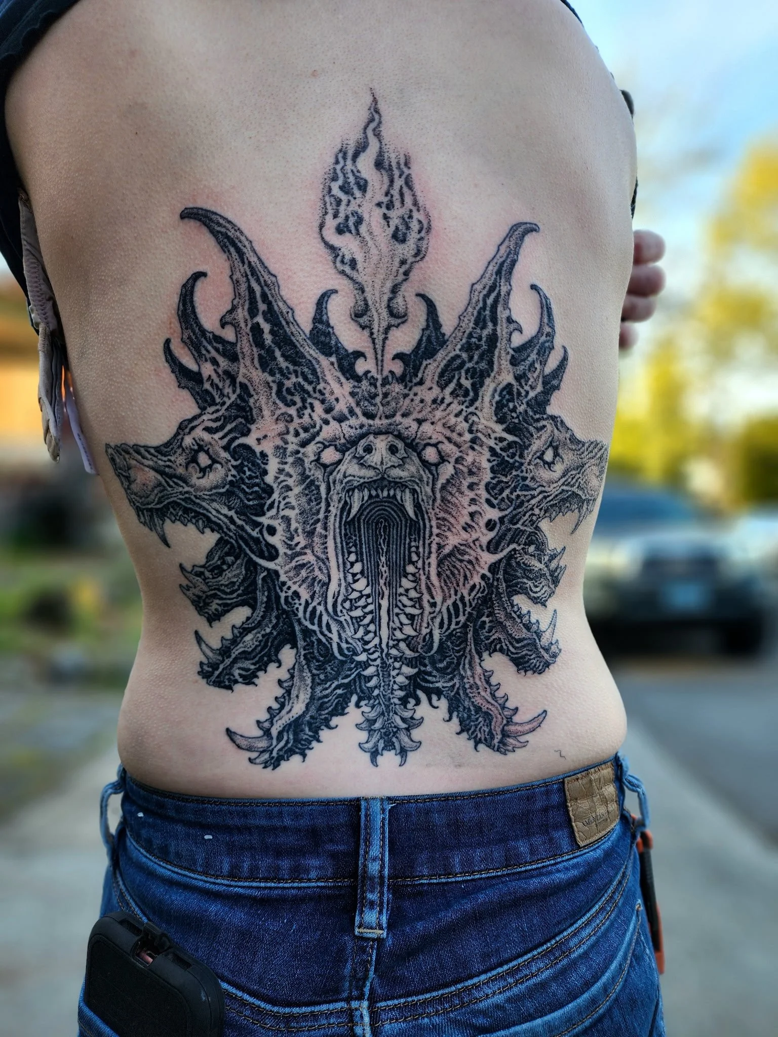 Tattoo of a fierce, multi-headed dragon on a person's torso, with detailed scales and open mouths showing teeth, inked in black.