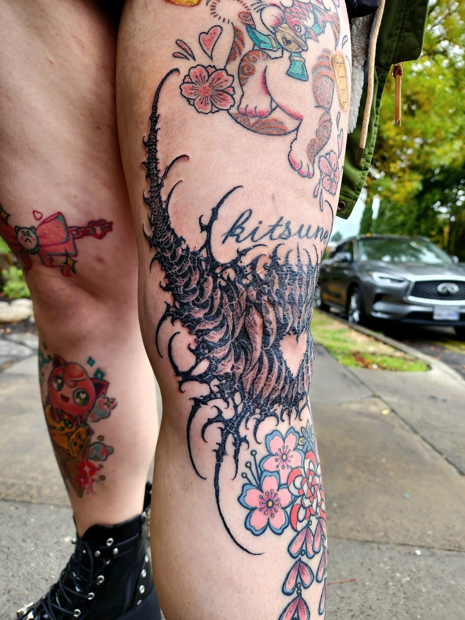 Various colorful tattoos on a person's arm and leg, including flowers, hearts, a character resembling a dog, and Japanese characters