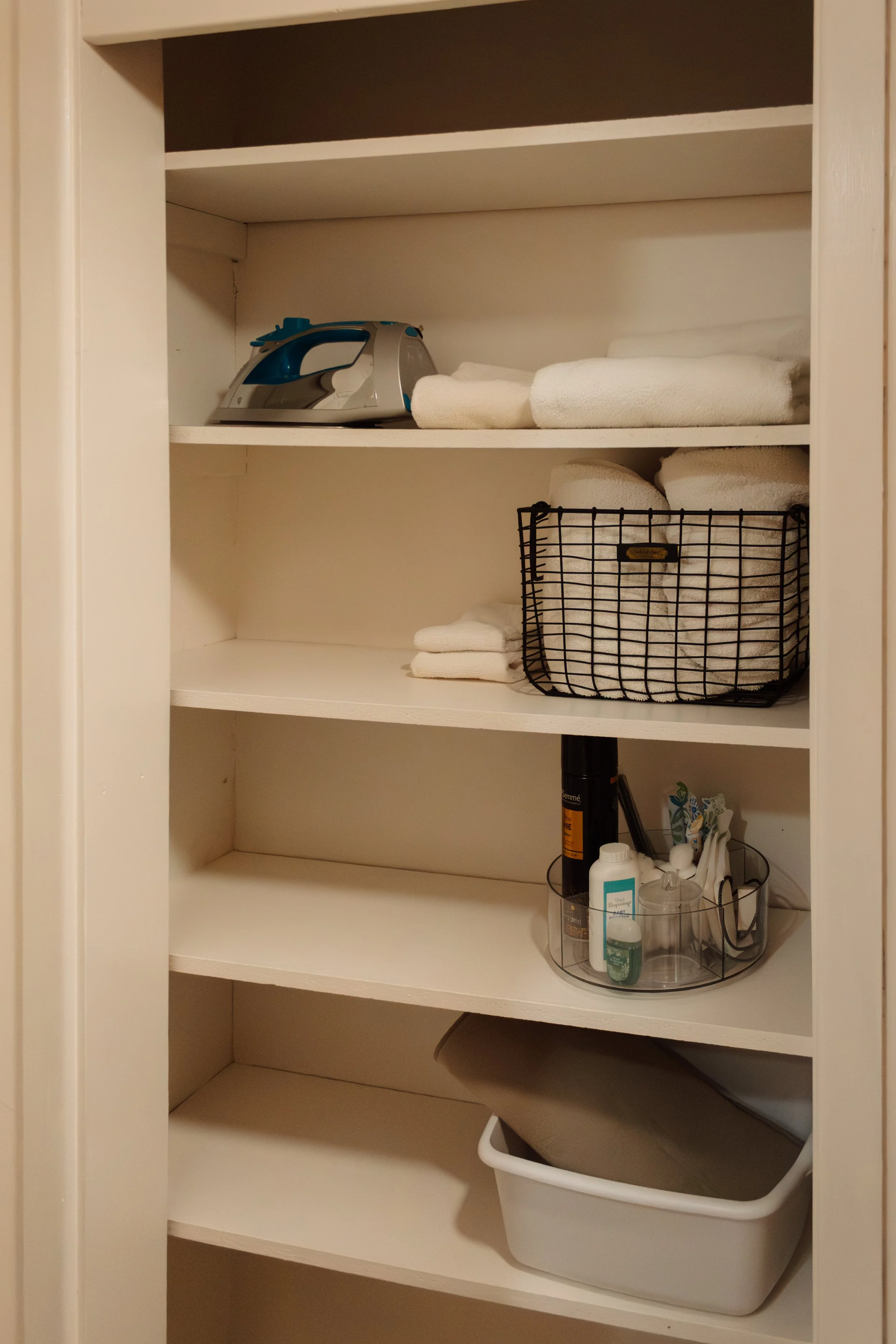 Empty white shelf cabinet with a few folded towels, cleaning supplies, and an iron.