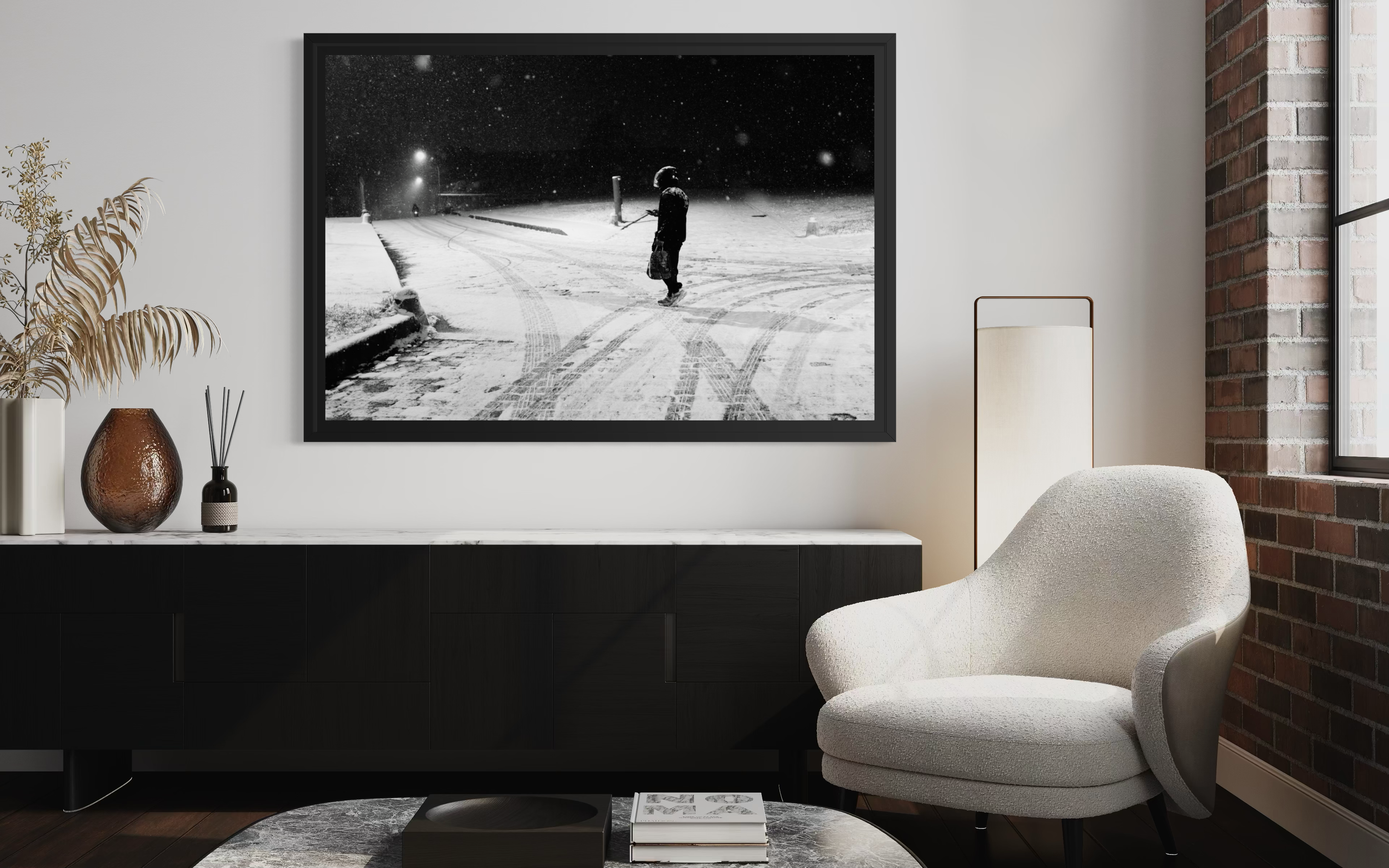 Photo en noir et blanc montrant une personne en manteau et bonnet marchant dans la neige, tenant un sac, dans un paysage nocturne avec neige, lampadaires et traces sur la neige.