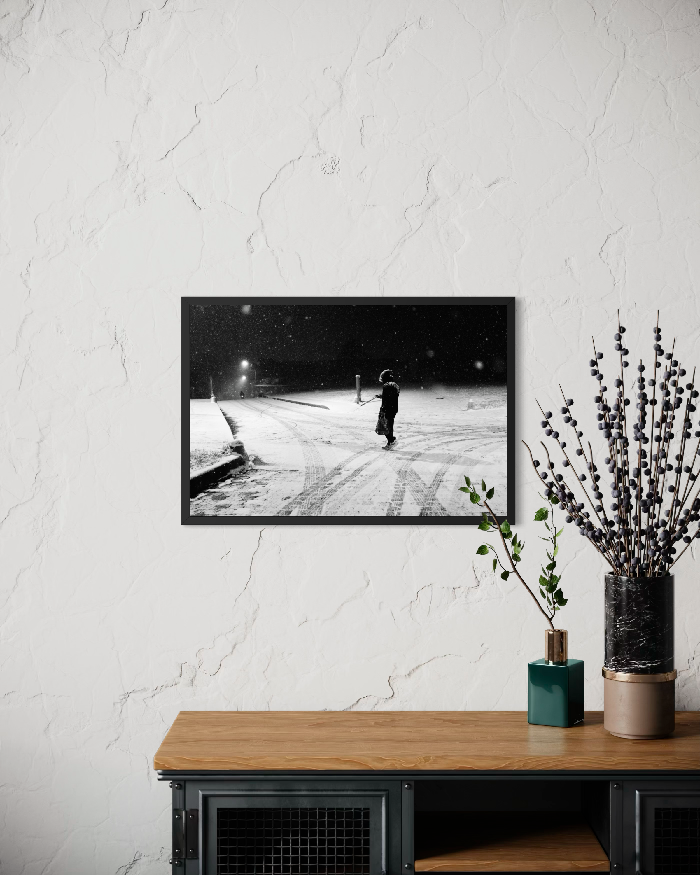 Une étagère en bois avec un tableau noir et une plante en pot en céramique. Le tableau noir montre une scène enneigée avec une personne avec un chapeau. La plante a des branches avec des baies foncées et des feuilles vertes.