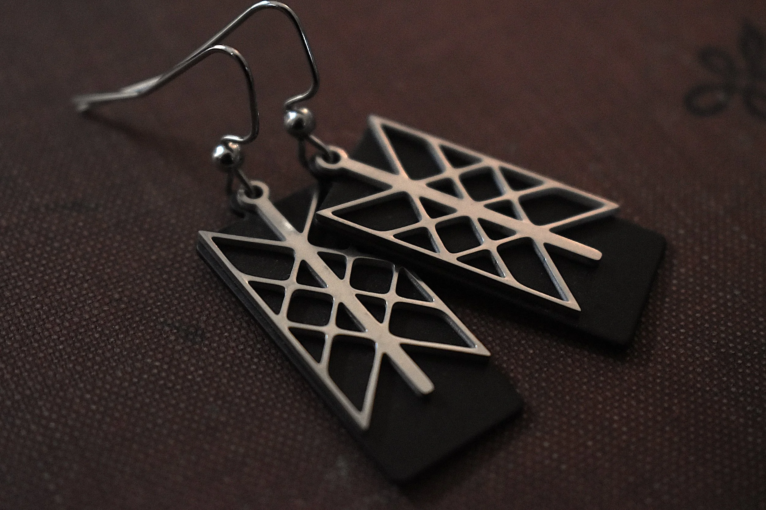 Handmade Web of Wyrd earrings featuring a silver charm on a black brass backing, symbolizing interconnectedness and fate.