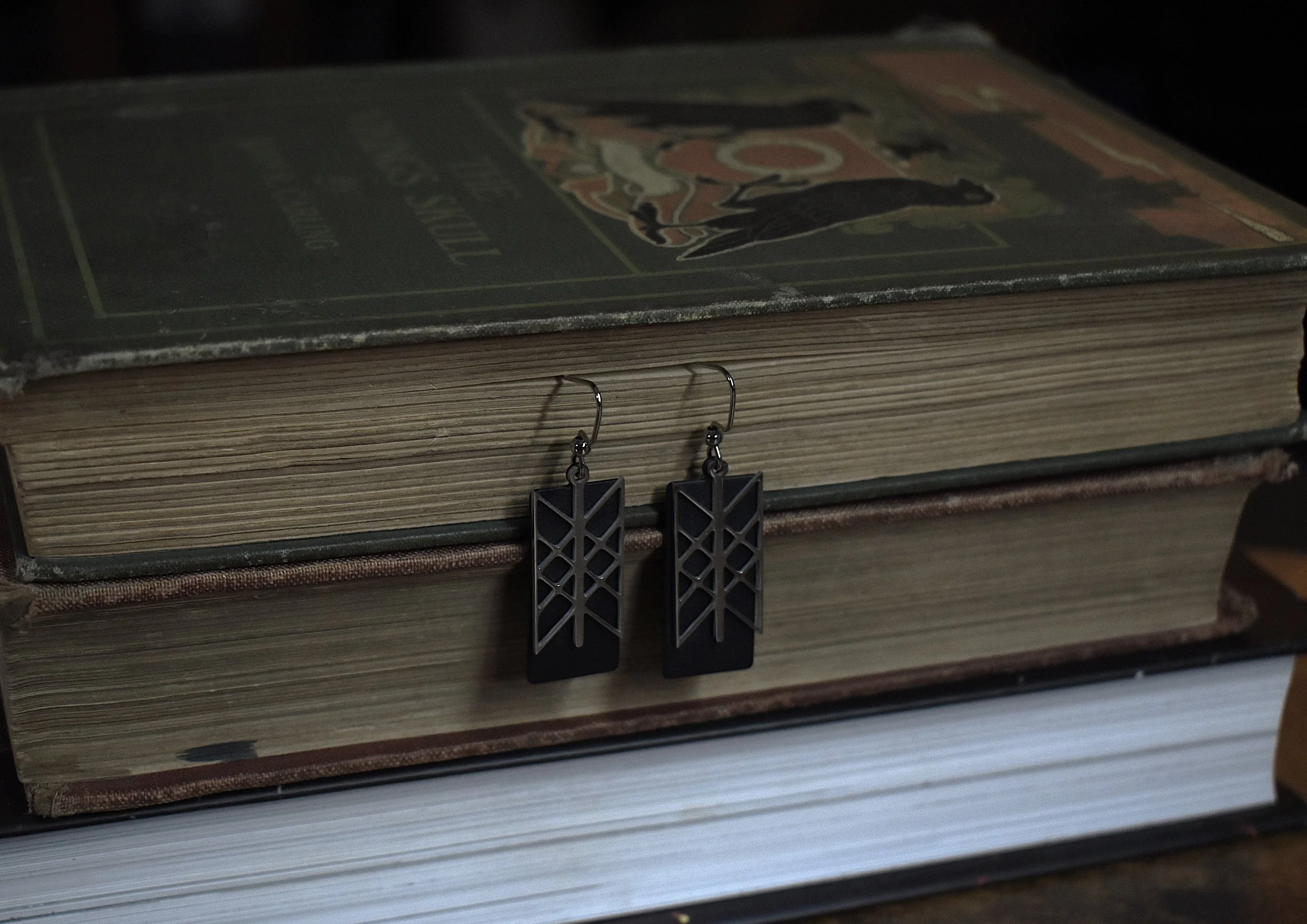 Handmade Web of Wyrd earrings featuring a silver charm on a black brass backing, symbolizing interconnectedness and fate.