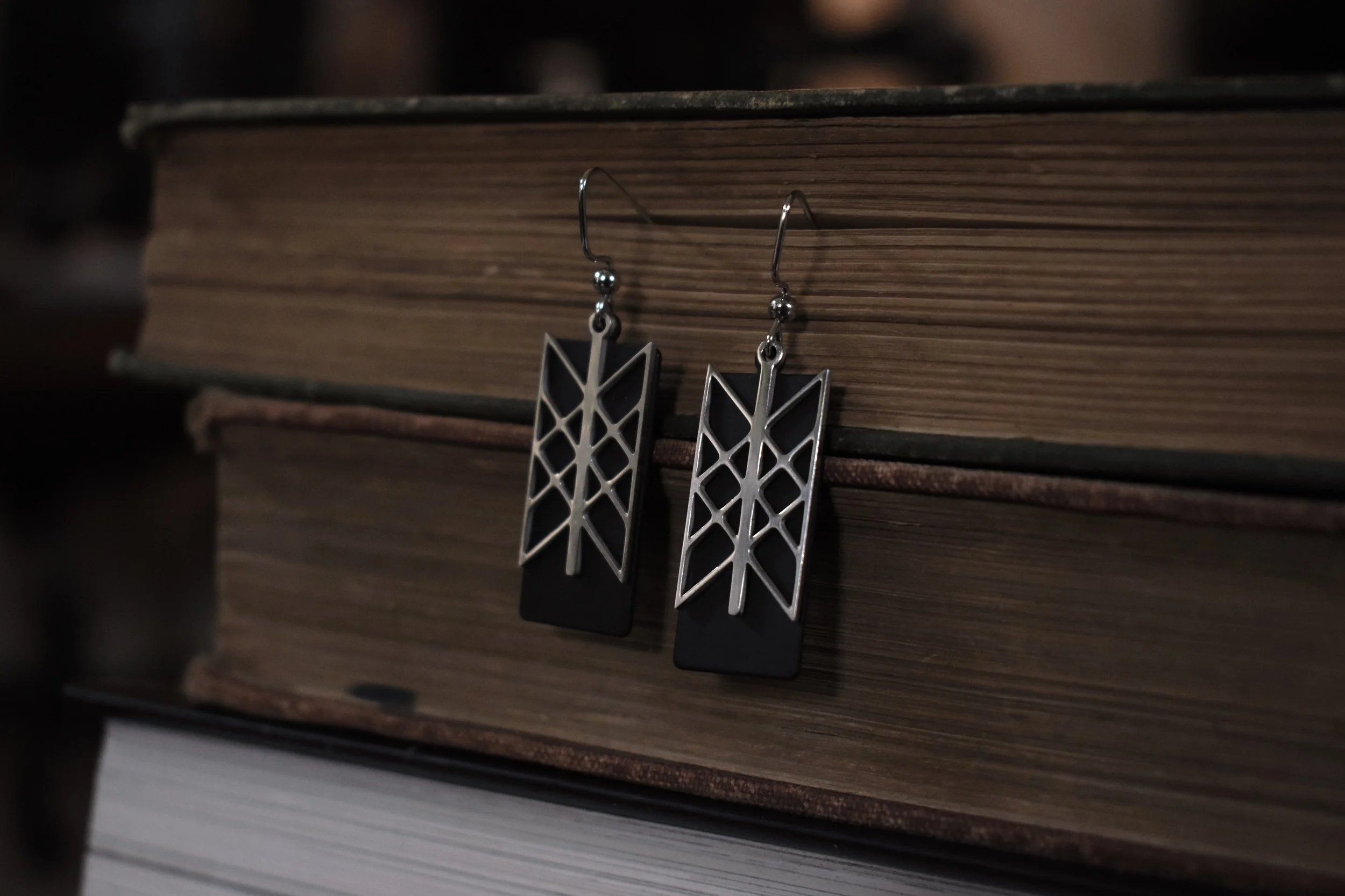 Handmade Web of Wyrd earrings featuring a silver charm on a black brass backing, symbolizing interconnectedness and fate.