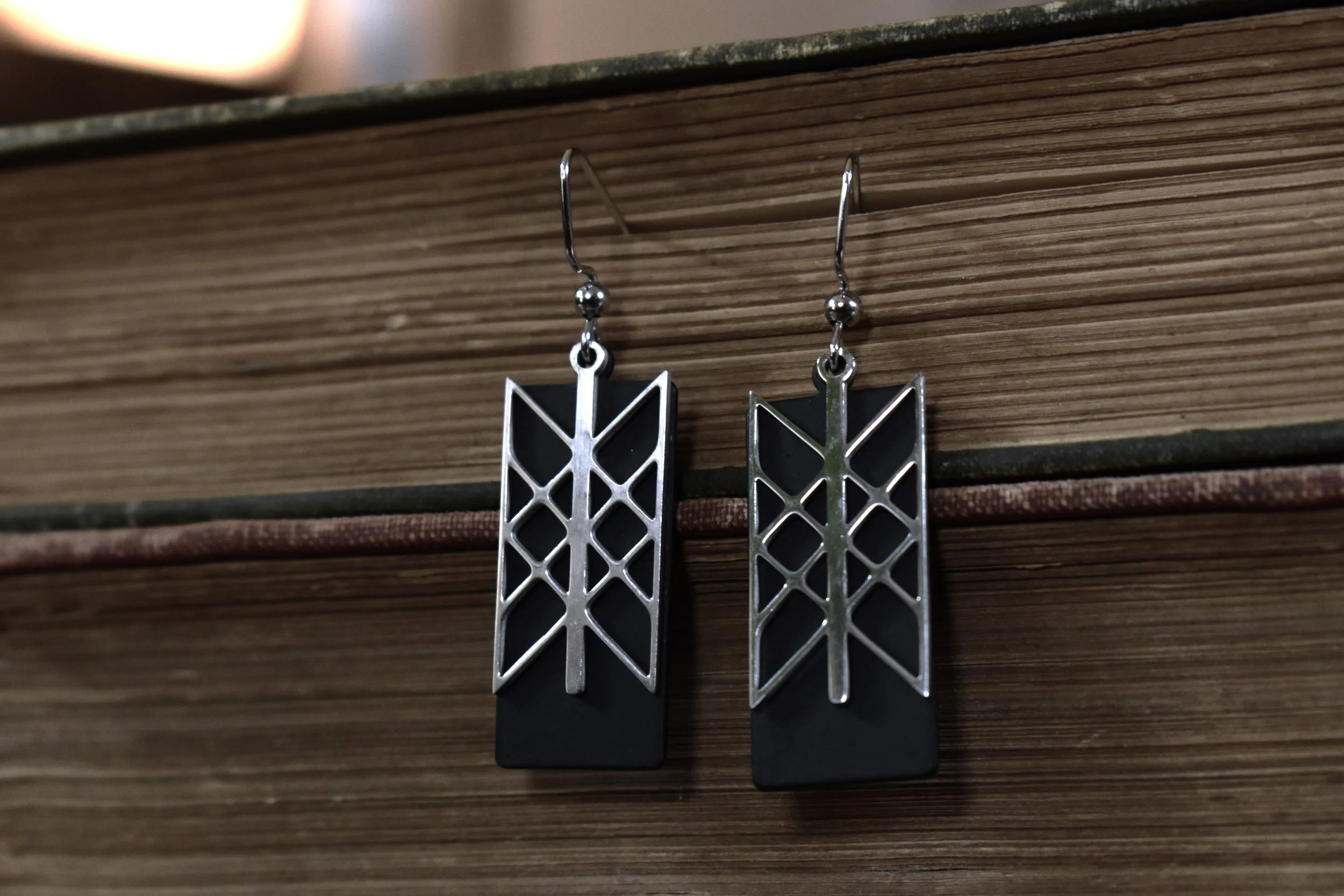 Handmade Web of Wyrd earrings featuring a silver charm on a black brass backing, symbolizing interconnectedness and fate.