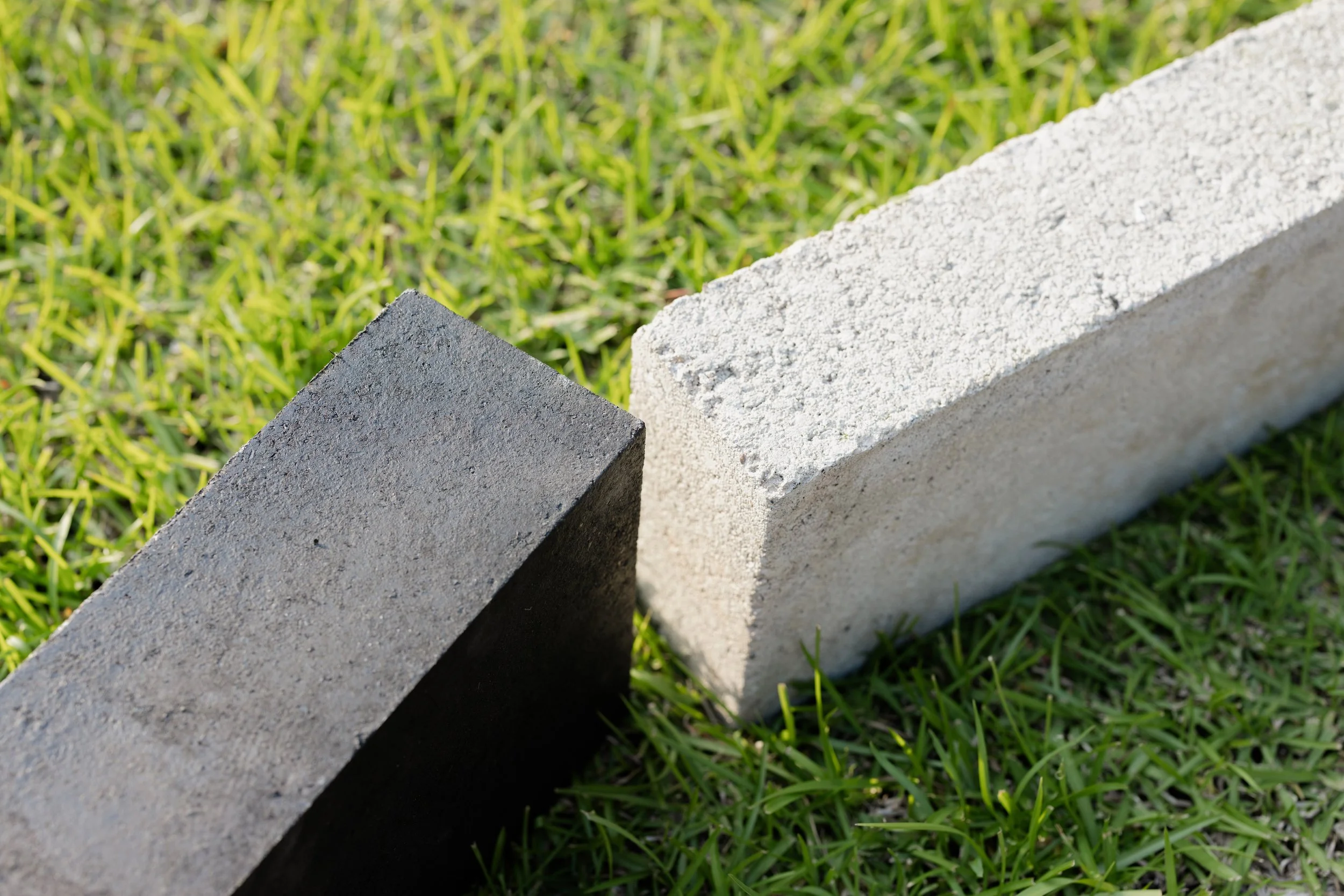 Close-up of a black concrete block and a light-colored concrete brick on green grass.