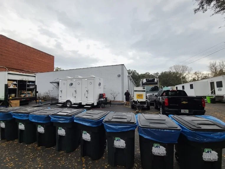 A parking lot with multiple trash bins, mobile office trailers, and recreational vehicles under a cloudy sky.