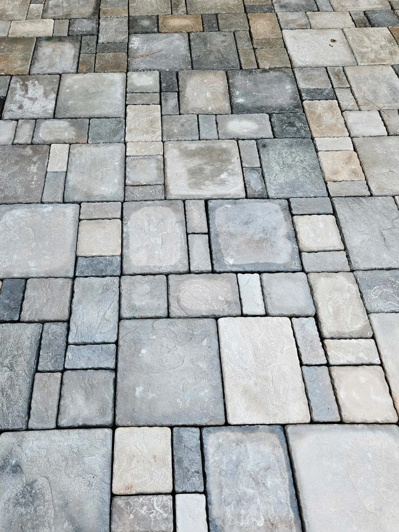 Patterned stone pavement with a mix of large and small rectangular and square stones in shades of gray and beige.