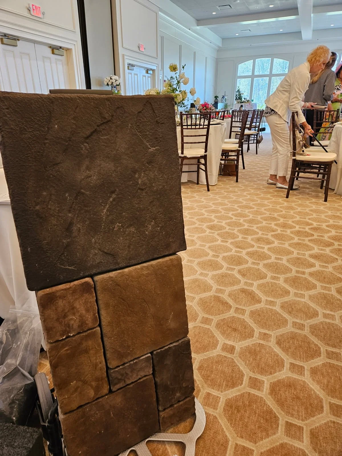 A stack of large textured stone tiles in front of a banquet hall with decorated tables and people setting up for an event.