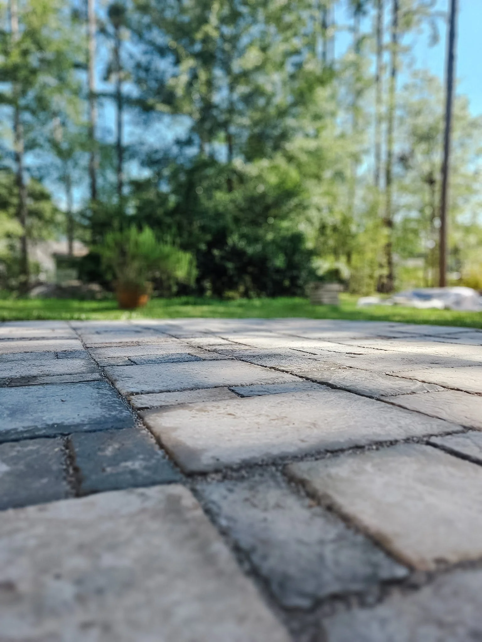 Close-up view of a stone brick patio with a blurred background of trees and a grassy yard on a sunny day.