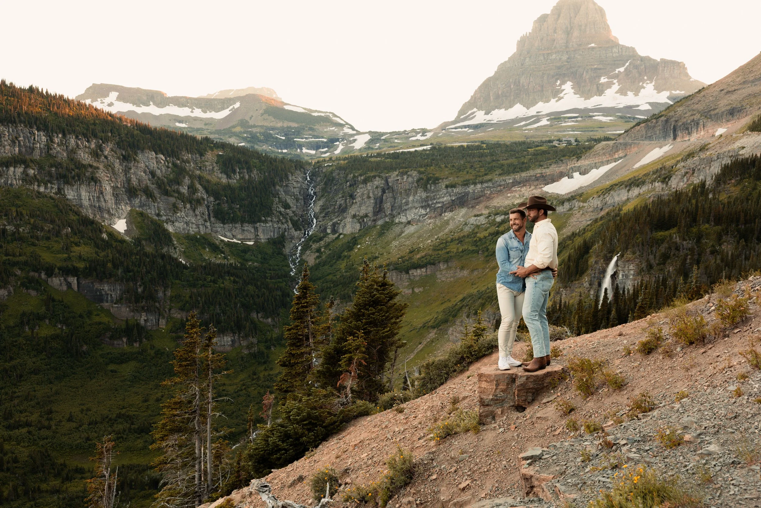 A couple stands against a scenic backdrop in Glacier National Park, Montana.