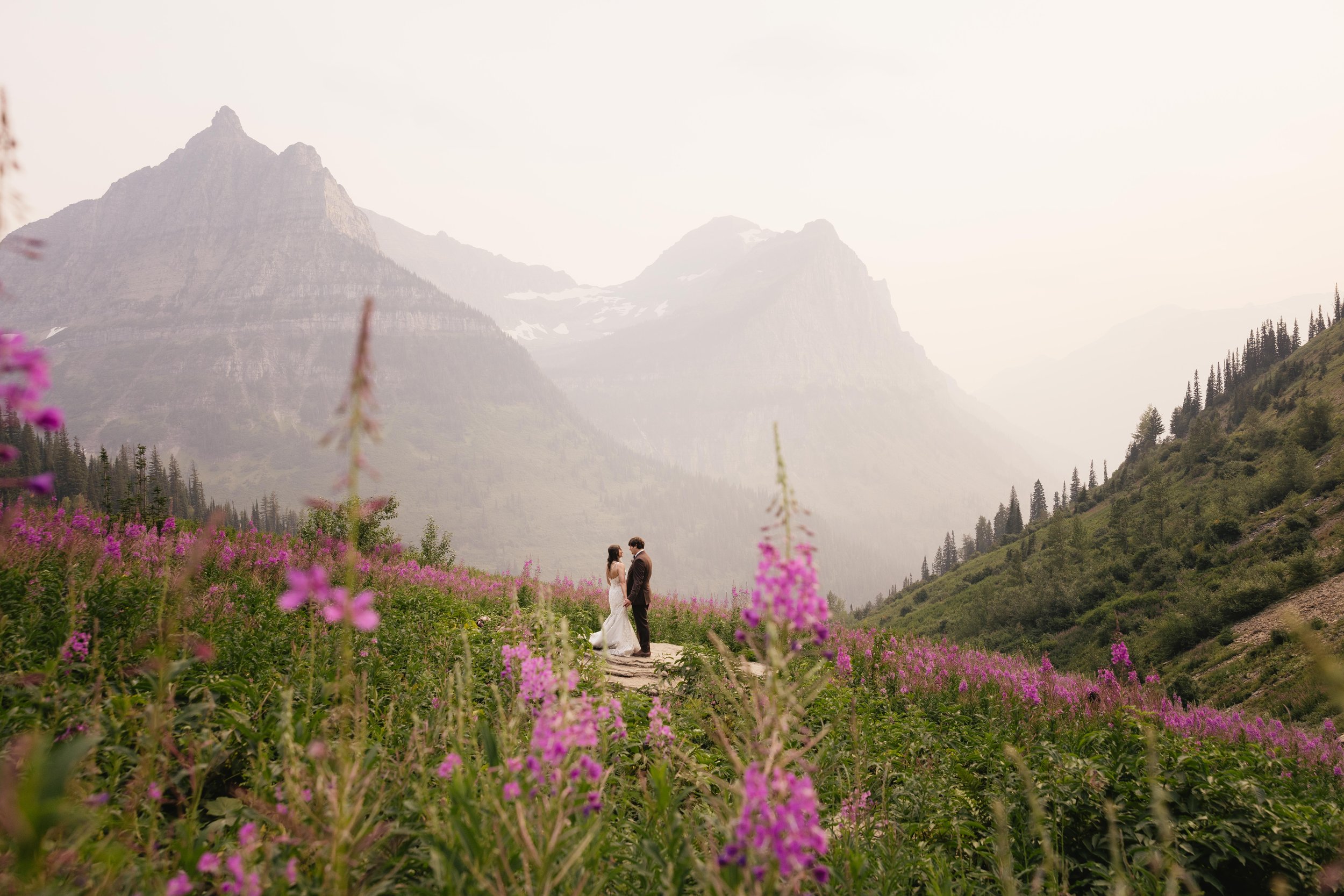 A couple stands in a meadow of fireweed flowers at Big Bend in Glacier National Park.