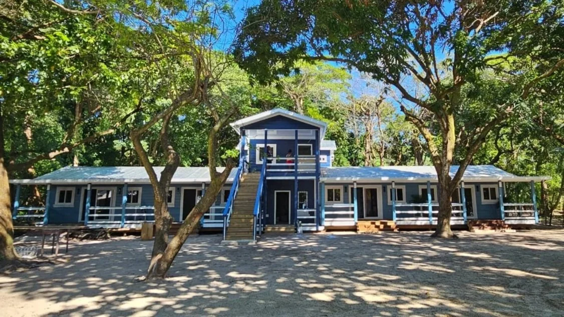 A blue, single-story building with an upper balcony surrounded by trees.