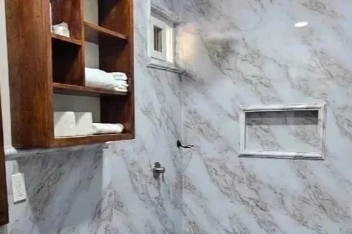 Modern bathroom with a marble shower, toilet, wooden vanity with a vessel sink, and wall-mounted shelving.