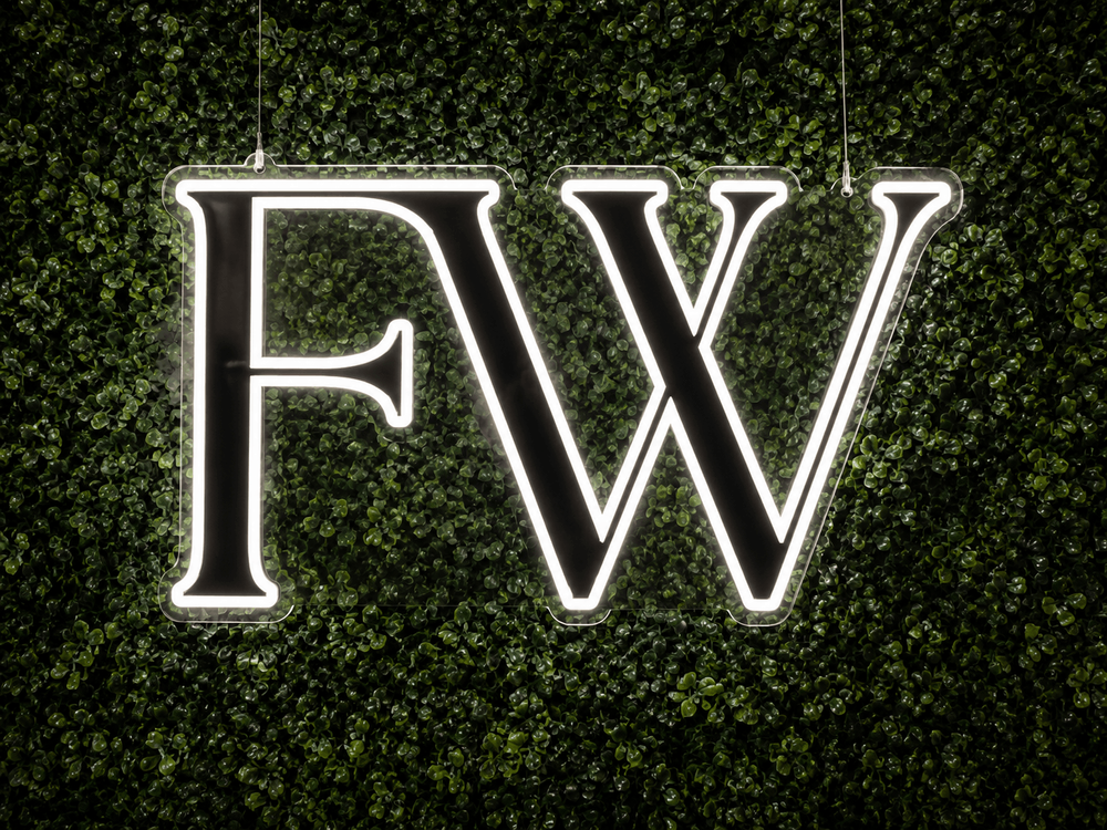 Custom Flower Walls of Nashville logo LED neon sign displayed on a boxwood greenery wall.