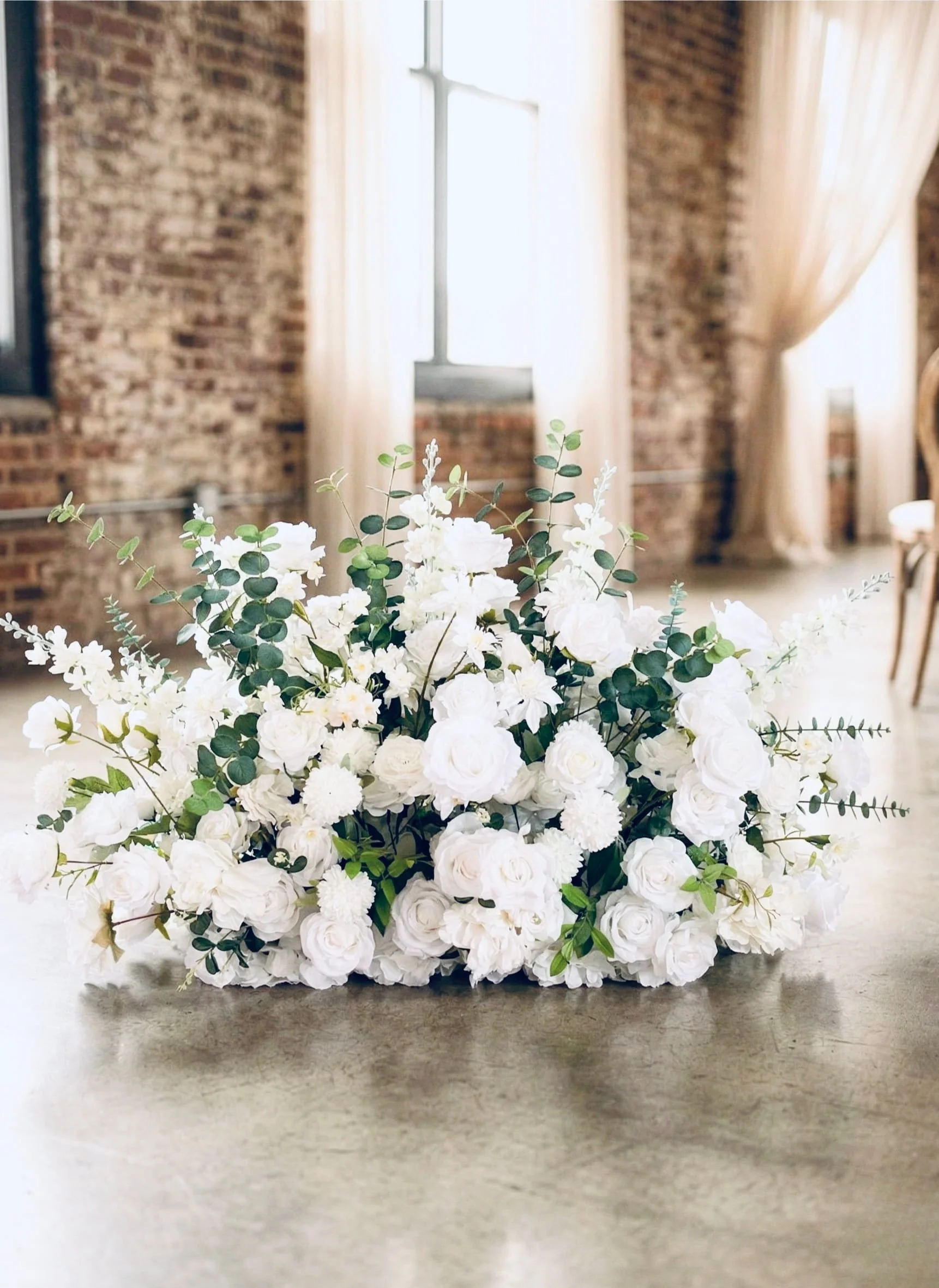 Floor-level white floral meadow arrangement rental for micro weddings and elopements in Nashville, featuring a lush mix of roses, mums, and eucalyptus, resting on polished concrete in an urban loft venue with exposed brick.