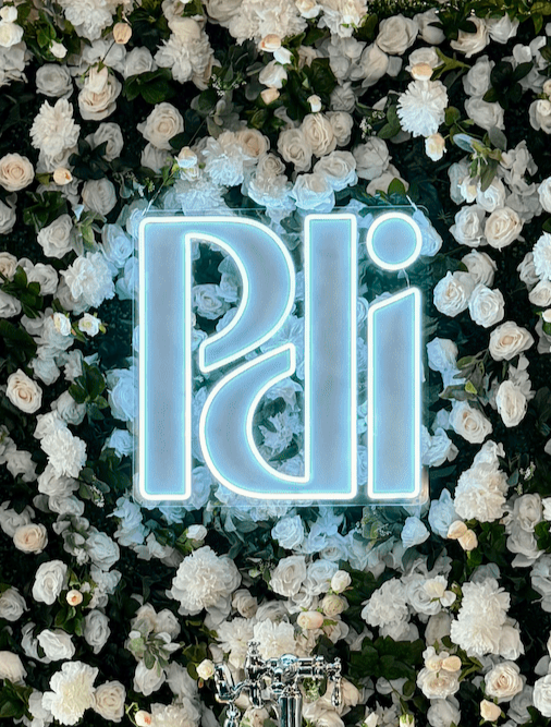 Custom PDI neon logo sign displayed on a white flower wall for an influencer event photo backdrop