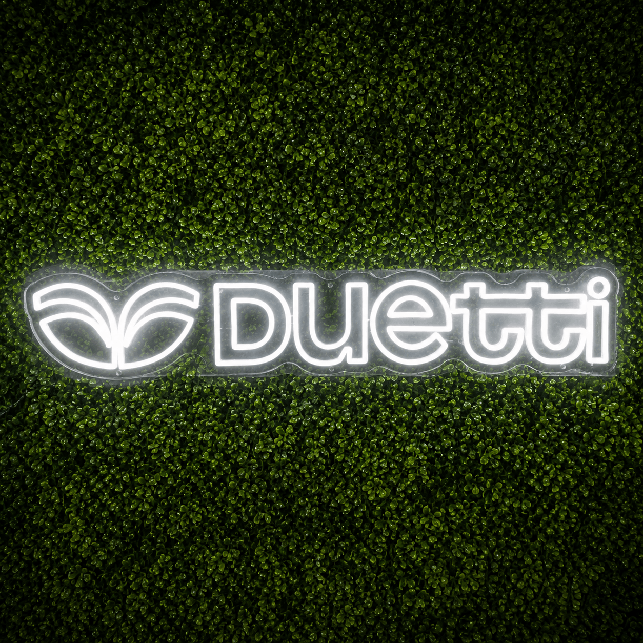 Custom Duetti logo LED neon sign on a green boxwood backdrop for a brand activation event